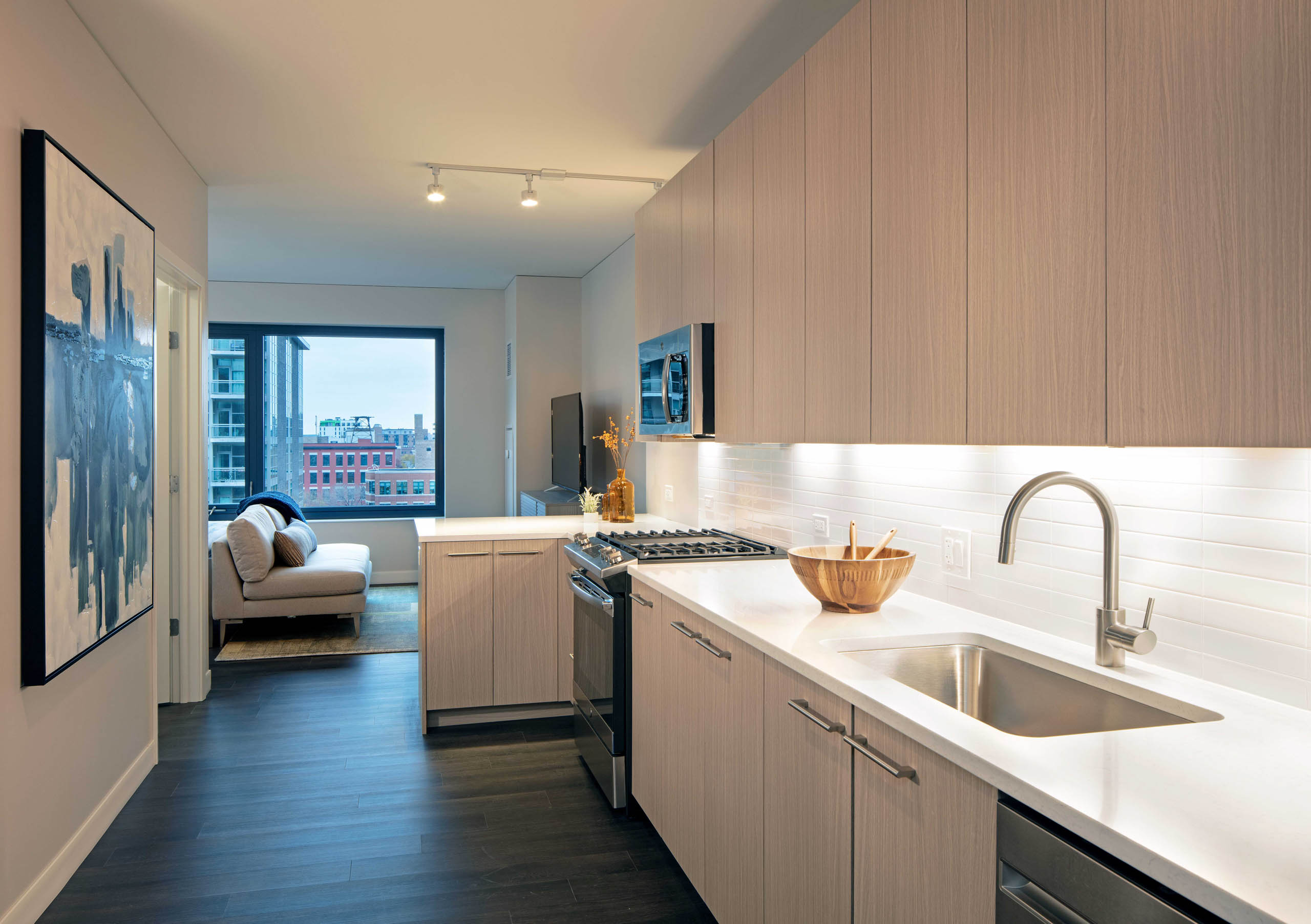 Kitchen with light wood cabinets and white tile backsplash with dark wood floors and view of  living space at AMLI West Loop