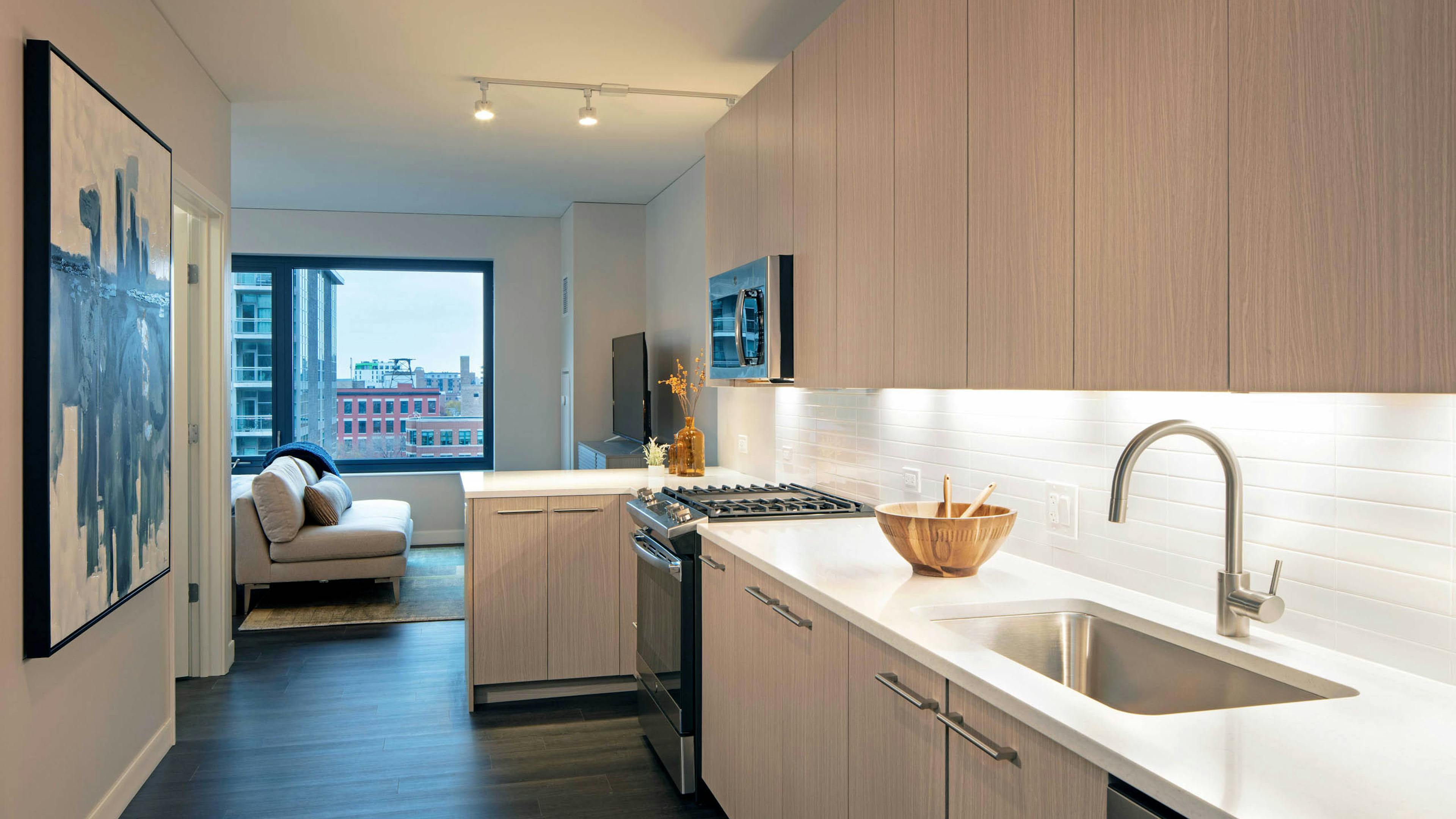 Kitchen with light wood cabinets and white tile backsplash with dark wood floors and view of  living space at AMLI West Loop