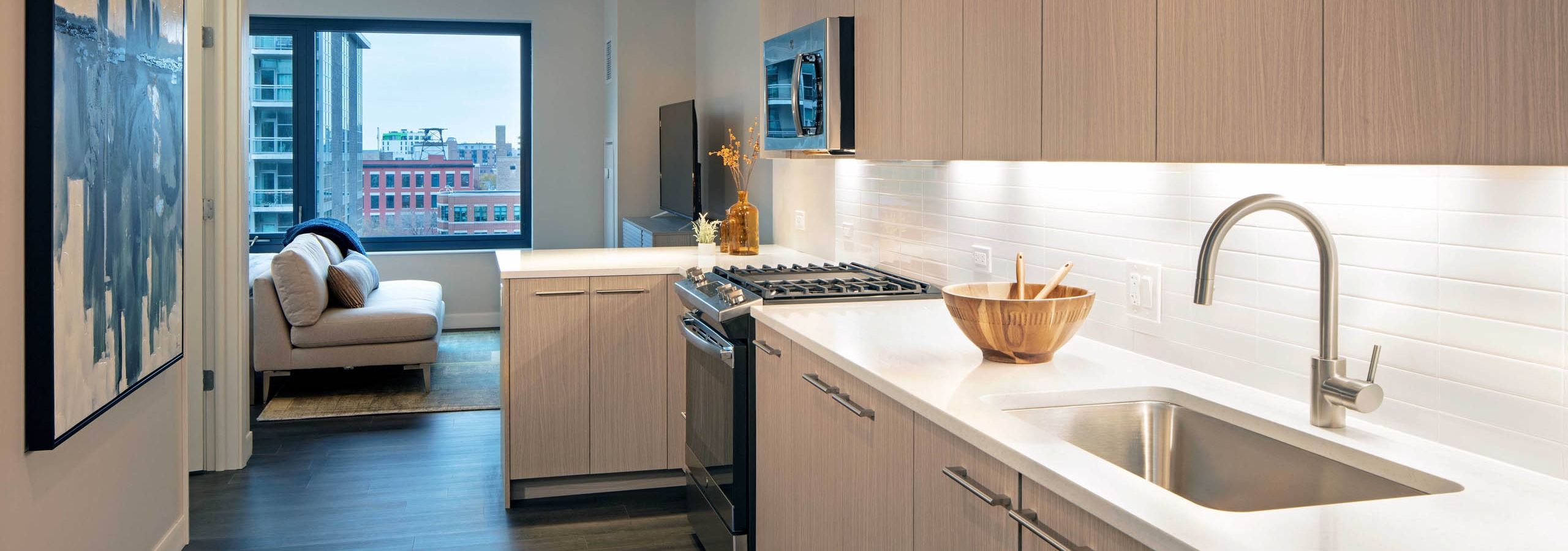 Kitchen with light wood cabinets and white tile backsplash with dark wood floors and view of living space at AMLI West Loop
