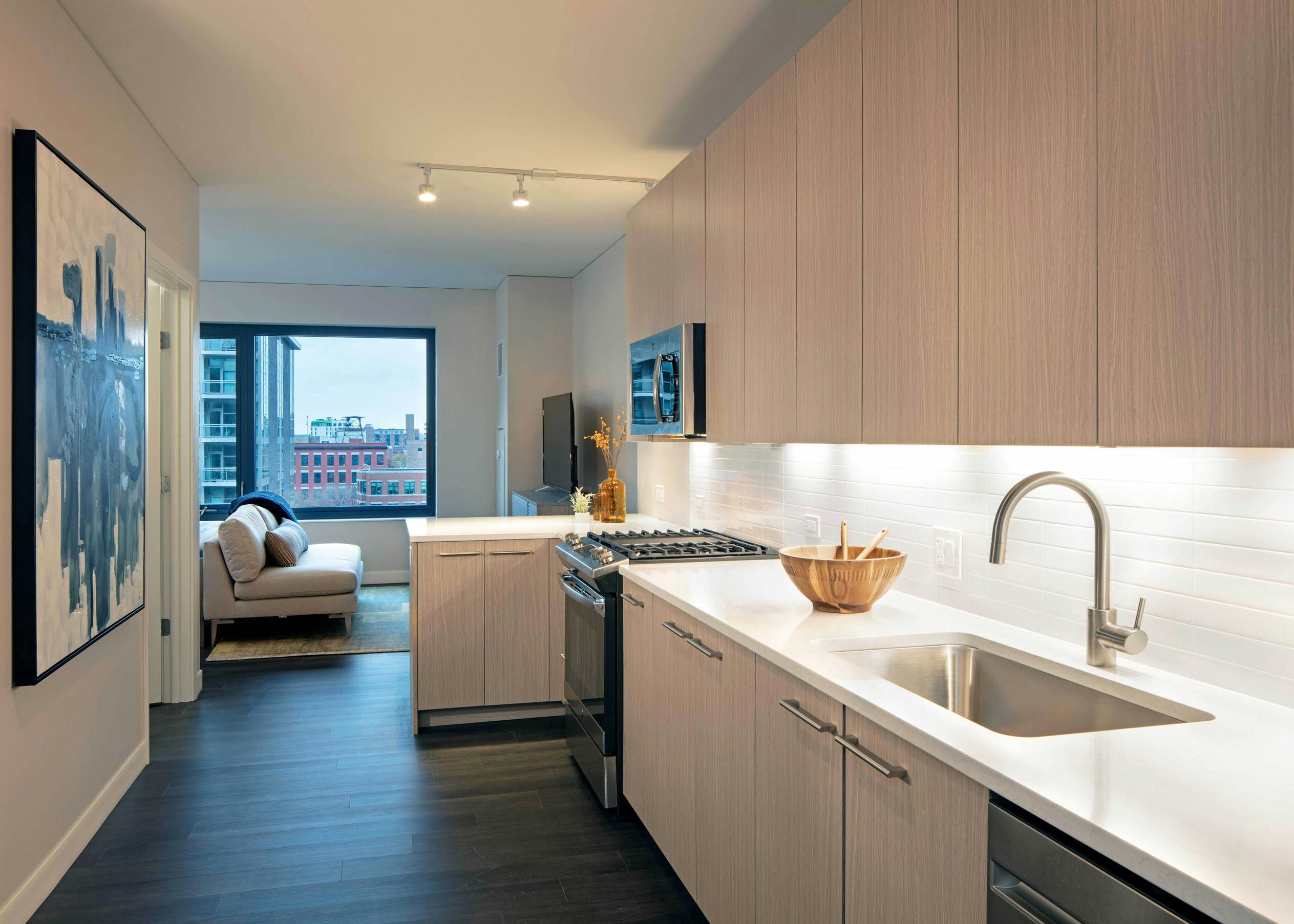 Kitchen with light wood cabinets and white tile backsplash with dark wood floors and view of living space at AMLI West Loop