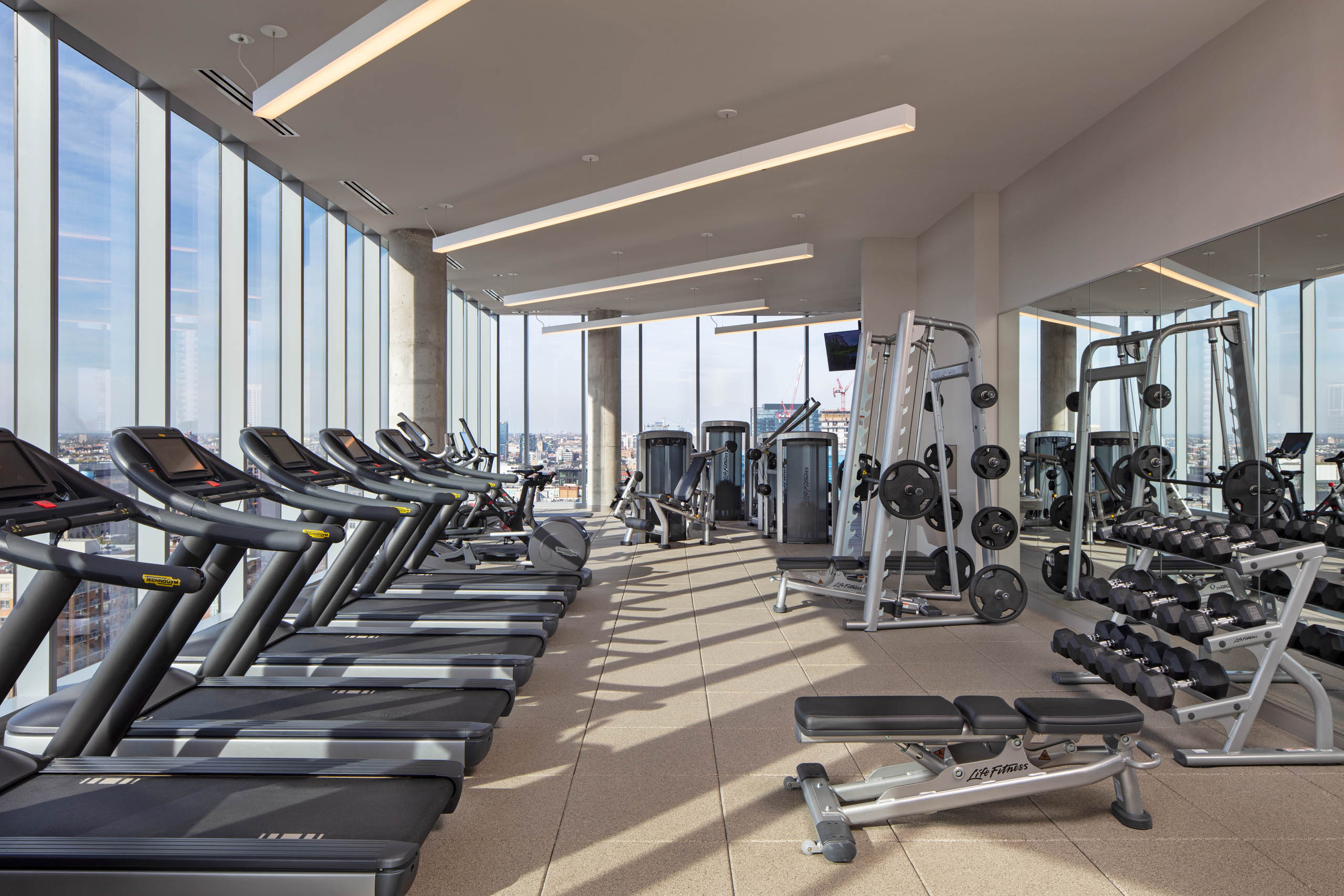 AMLI West Loop fitness center surrounded by large windows and exercise machines facing Chicago skyline view