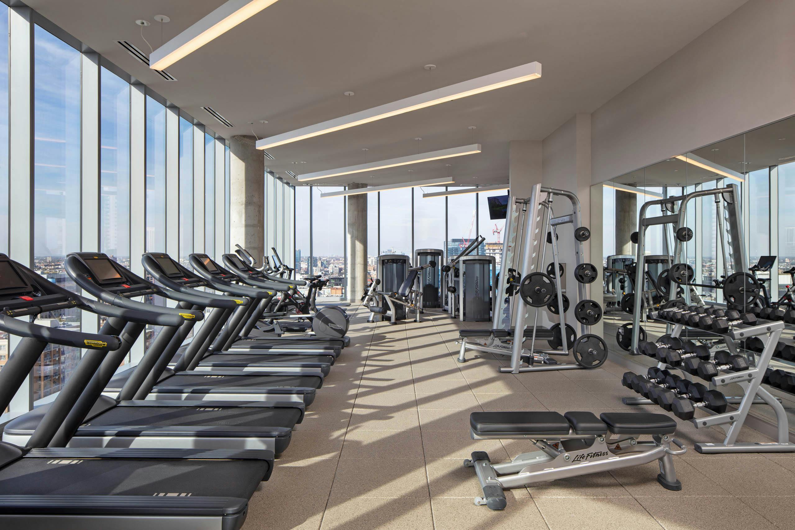 AMLI West Loop fitness center surrounded by large windows and exercise machines facing Chicago skyline view