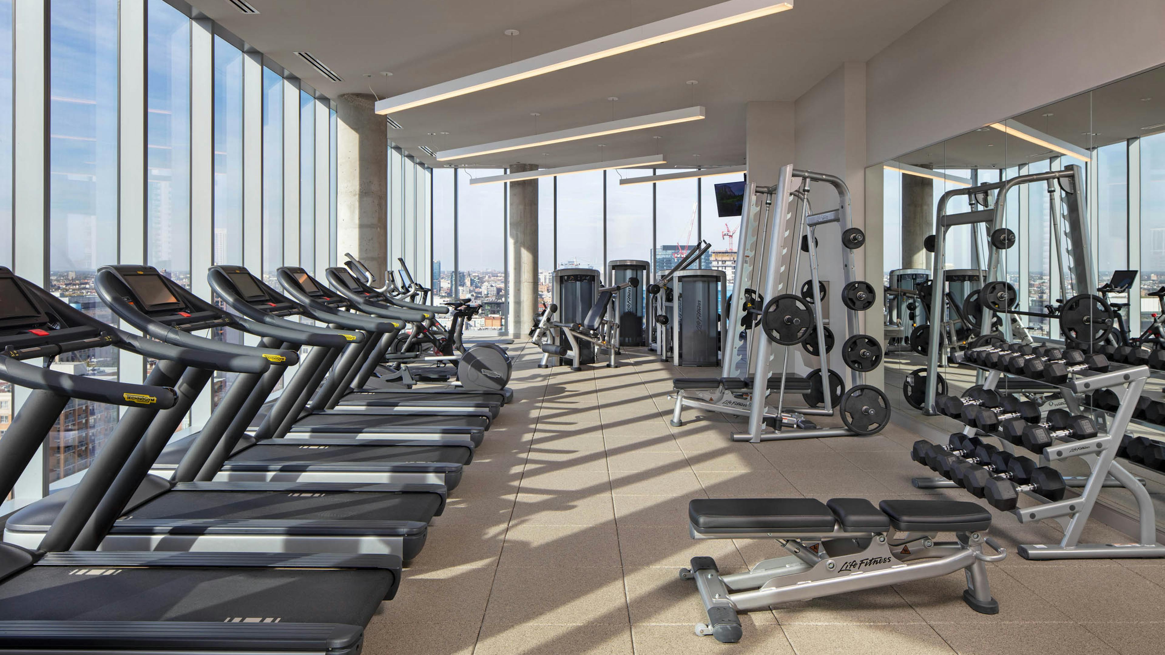 AMLI West Loop fitness center surrounded by large windows and exercise machines facing Chicago skyline view