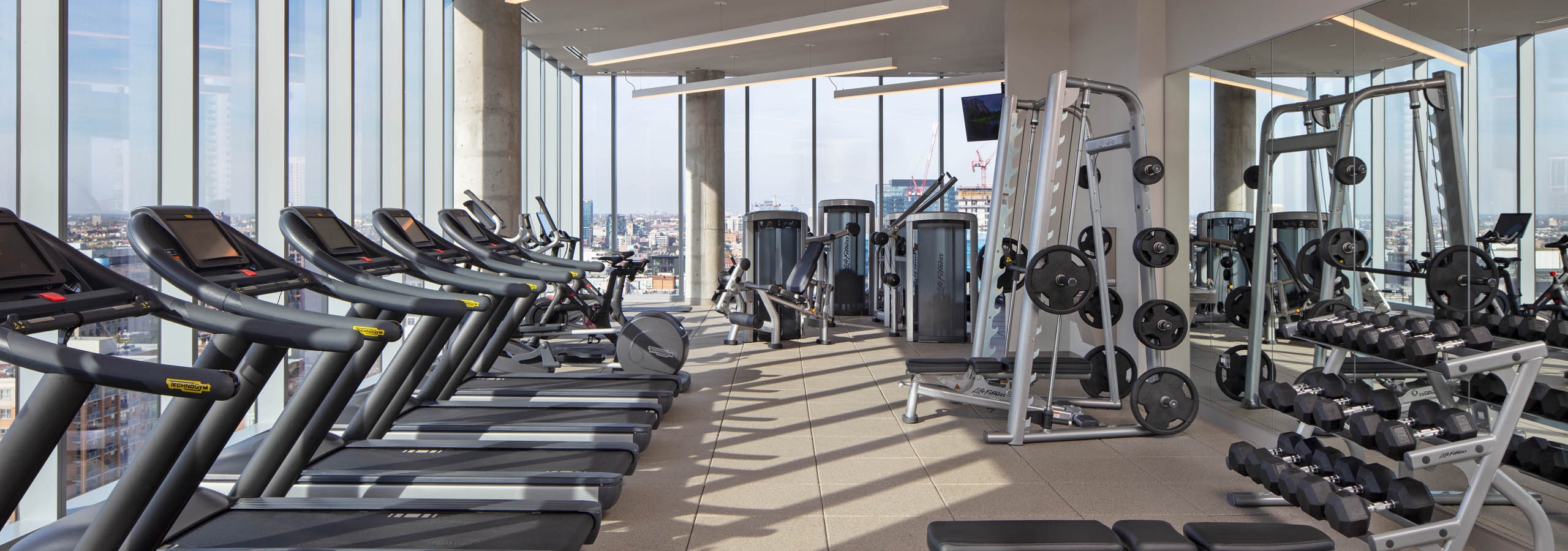 AMLI West Loop fitness center surrounded by large windows and exercise machines facing Chicago skyline view