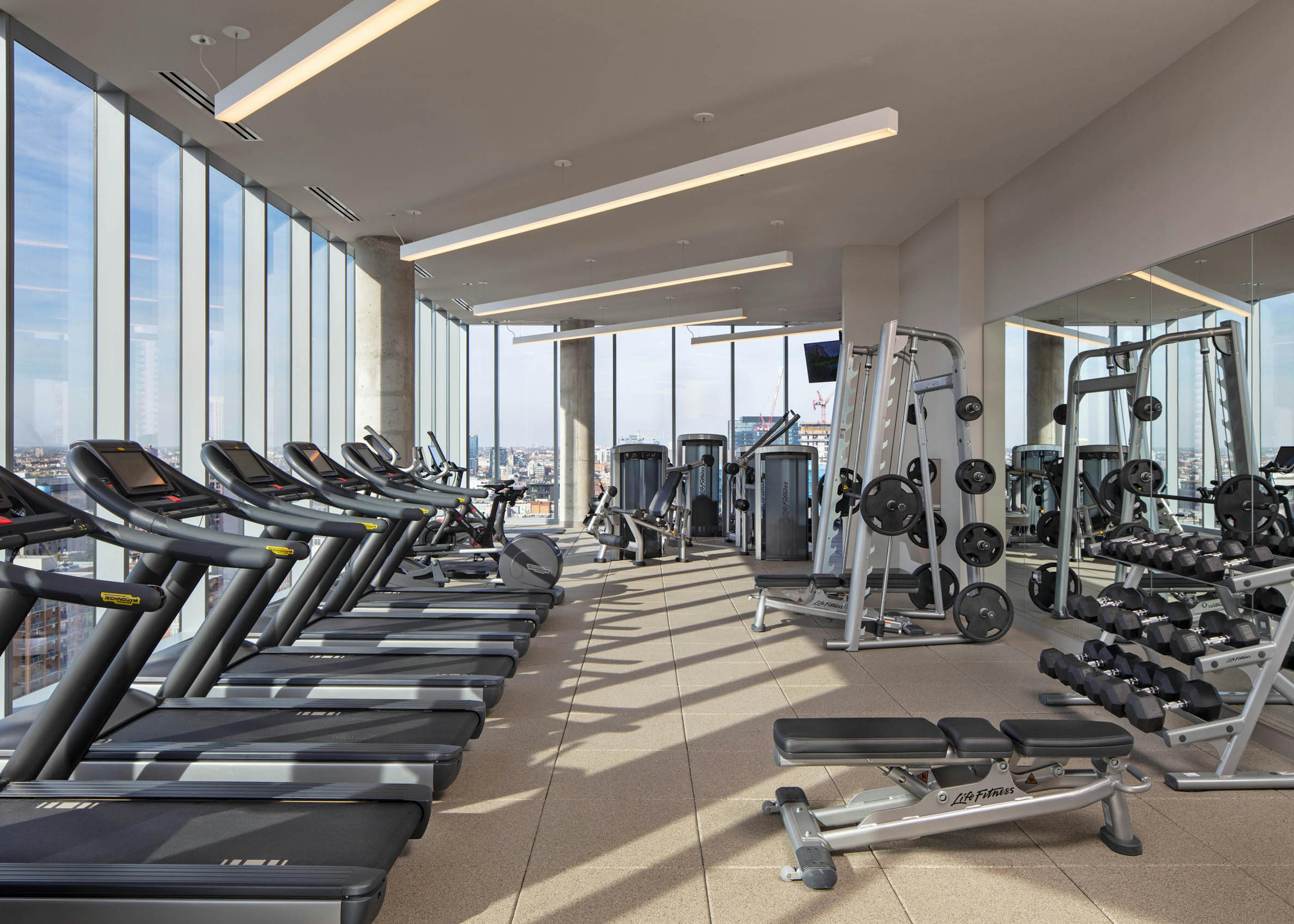 AMLI West Loop fitness center surrounded by large windows and exercise machines facing Chicago skyline view