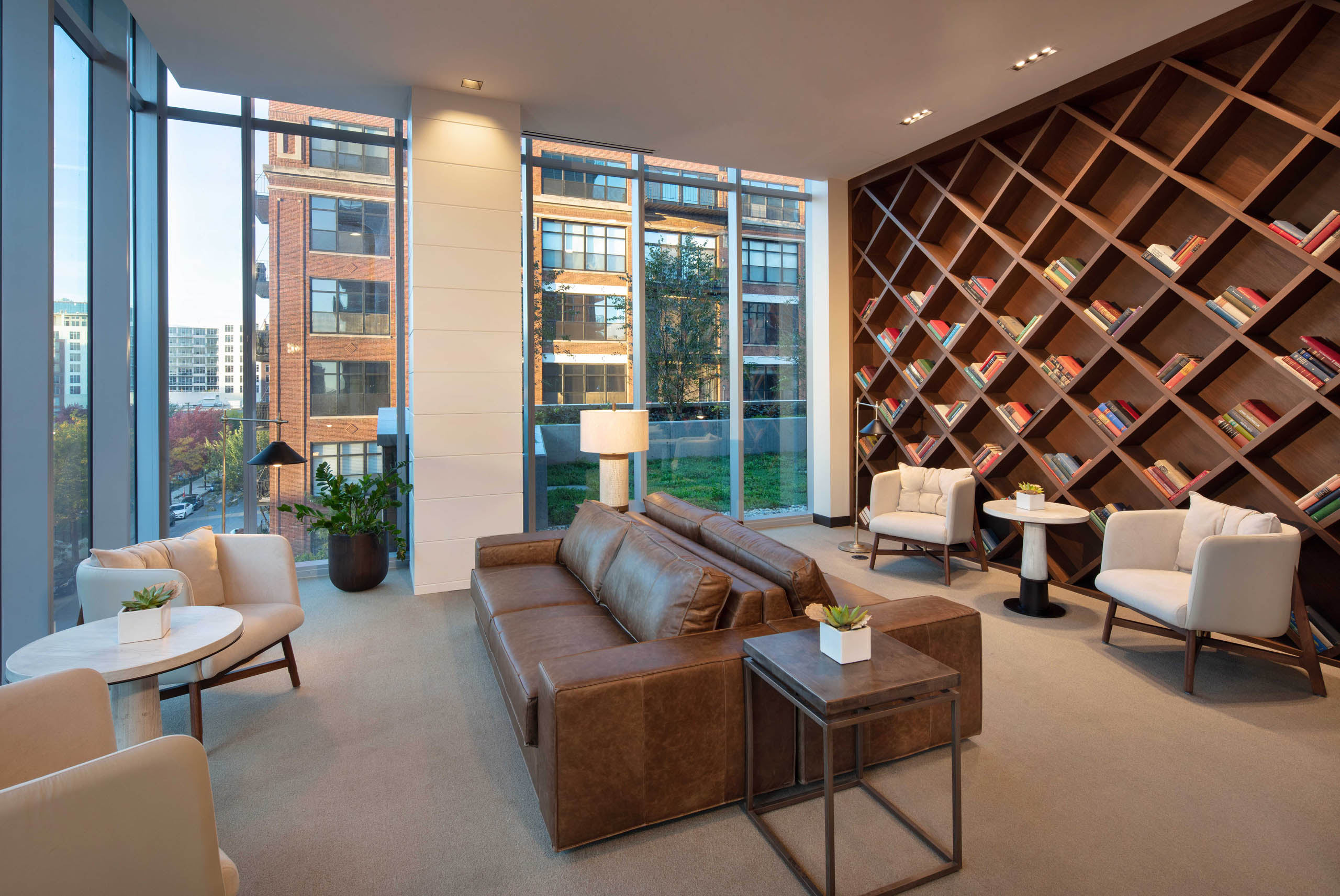 Interior shot of modern library with brown leather couches, white chairs, and a large wooden bookcase