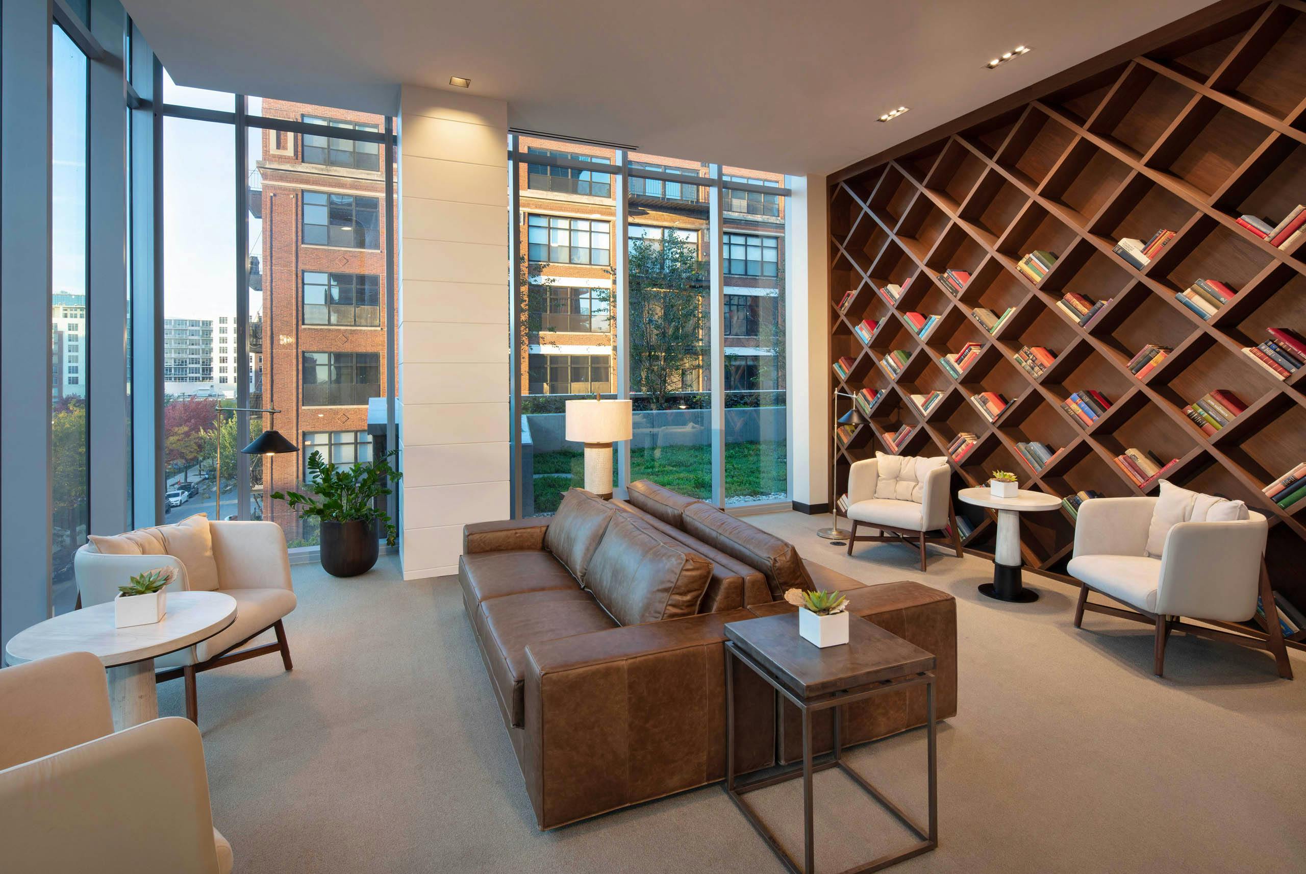 Interior shot of modern library with brown leather couches, white chairs, and a large wooden bookcase