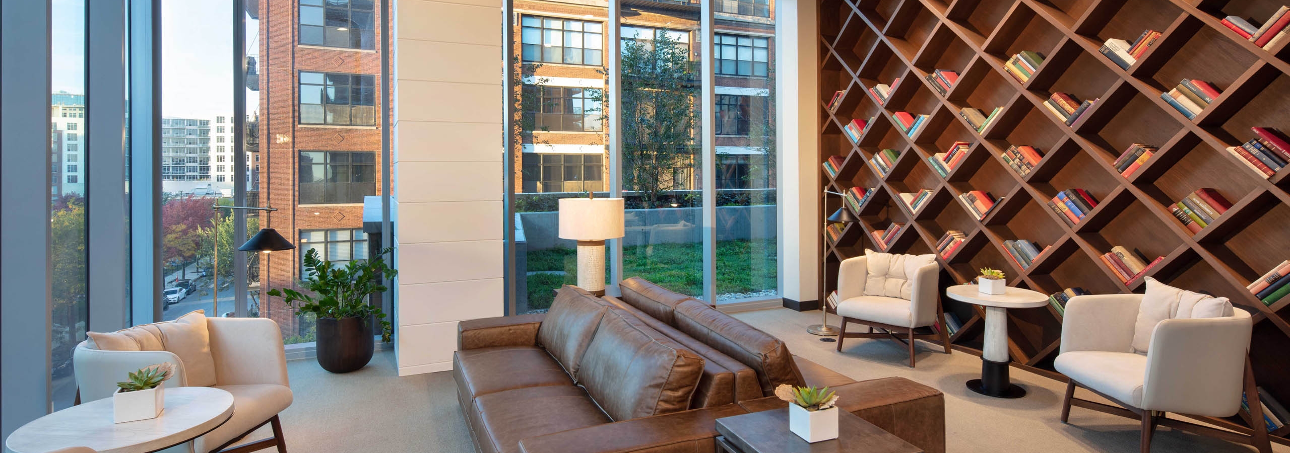 Interior shot of modern library with brown leather couches, white chairs, and a large wooden bookcase