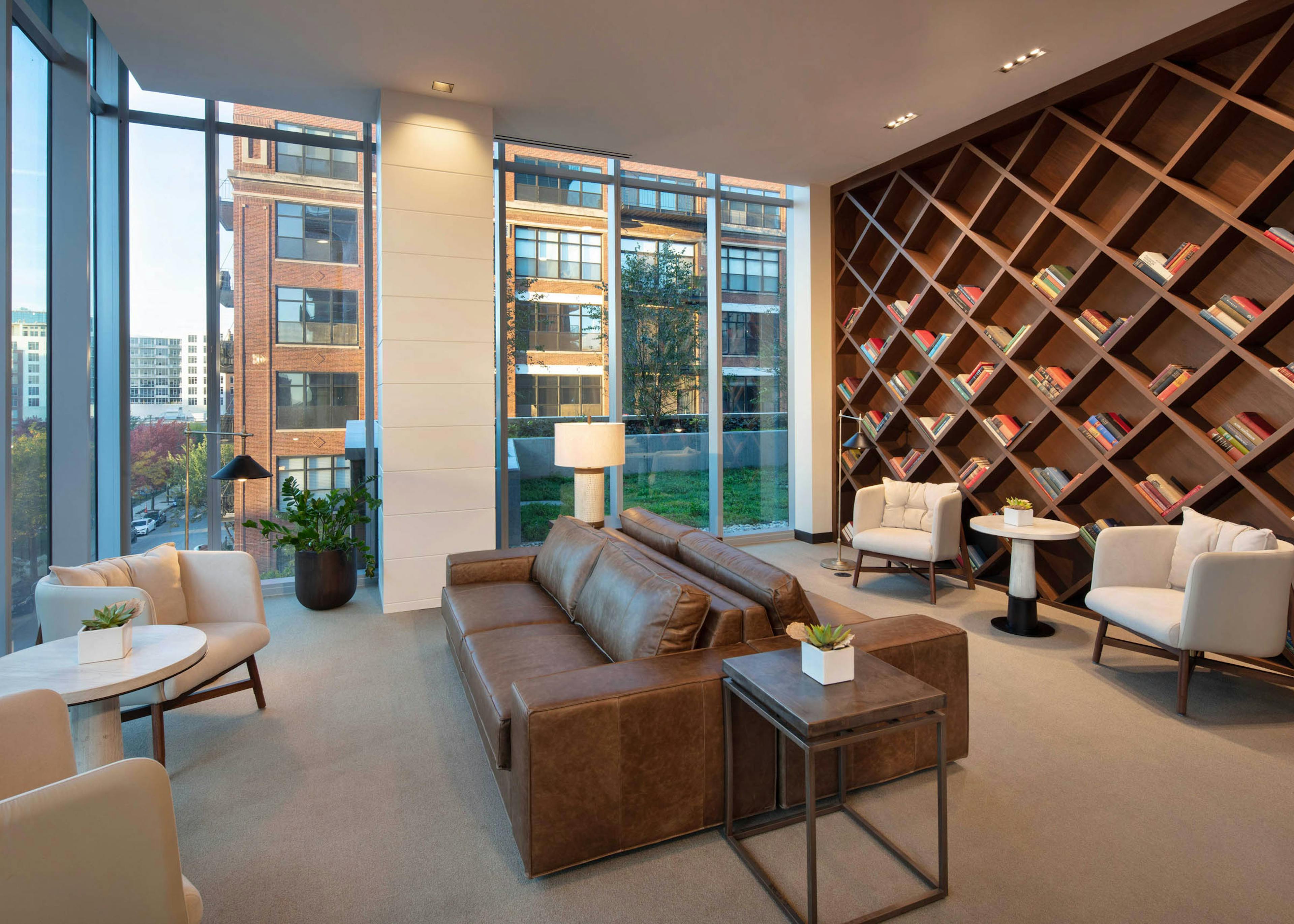 Interior shot of modern library with brown leather couches, white chairs, and a large wooden bookcase
