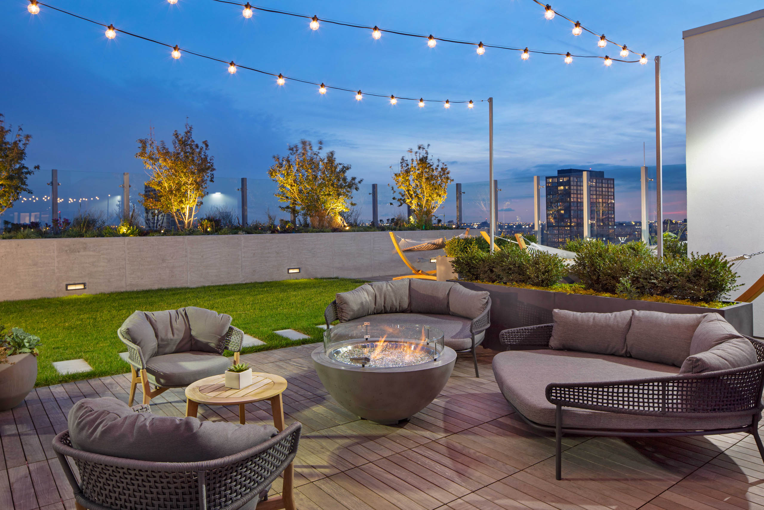 Nighttime view of rooftop firepits with grey lounge seating and string lights at AMLI West Loop