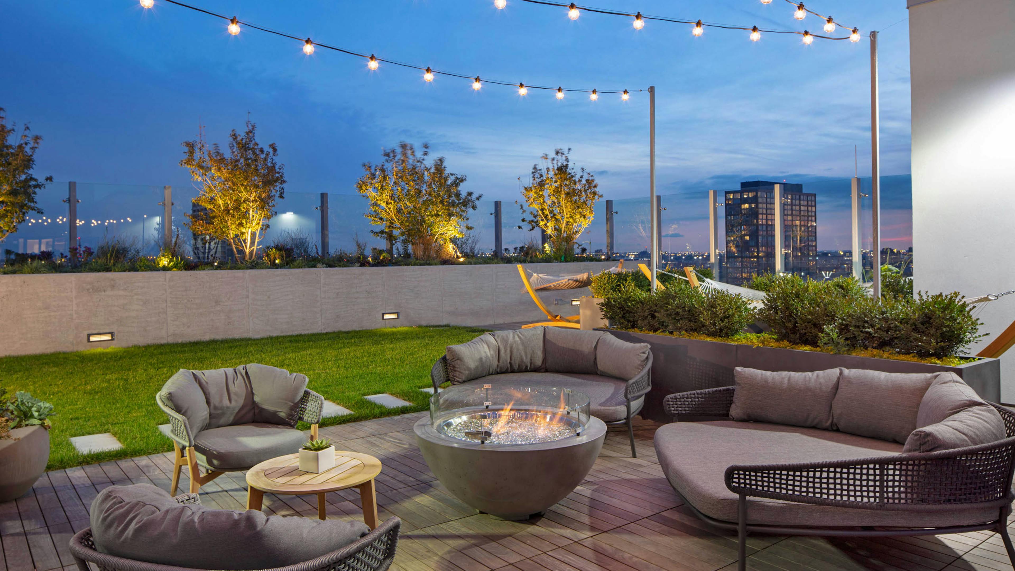 Nighttime view of rooftop firepits with grey lounge seating and string lights at AMLI West Loop