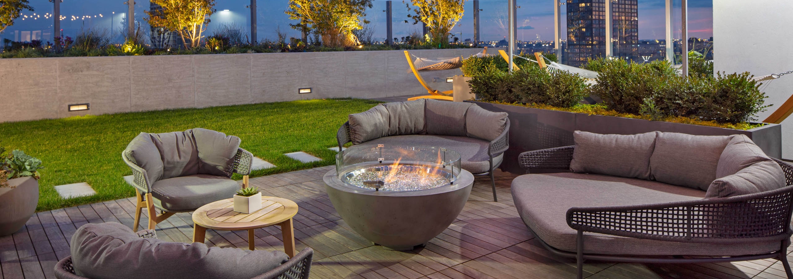 Nighttime view of rooftop firepits with grey lounge seating and string lights at AMLI West Loop