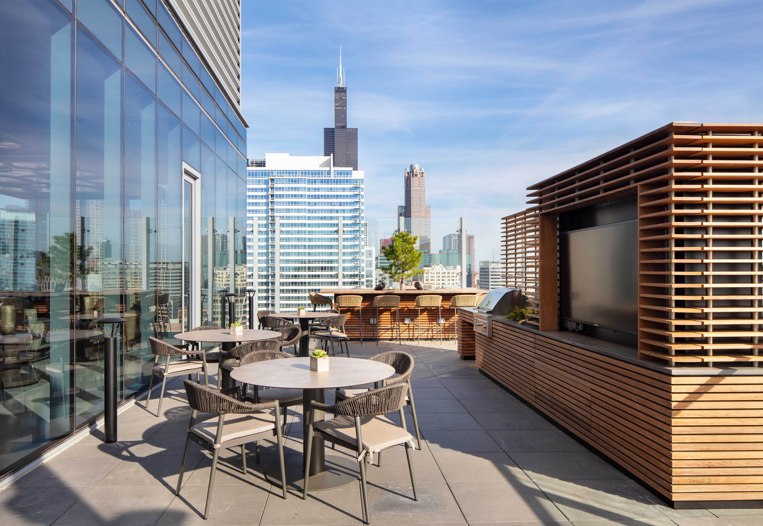 AMLI West Loop spacious rooftop dining area with tables, a grill station, and a view of the city skyline.