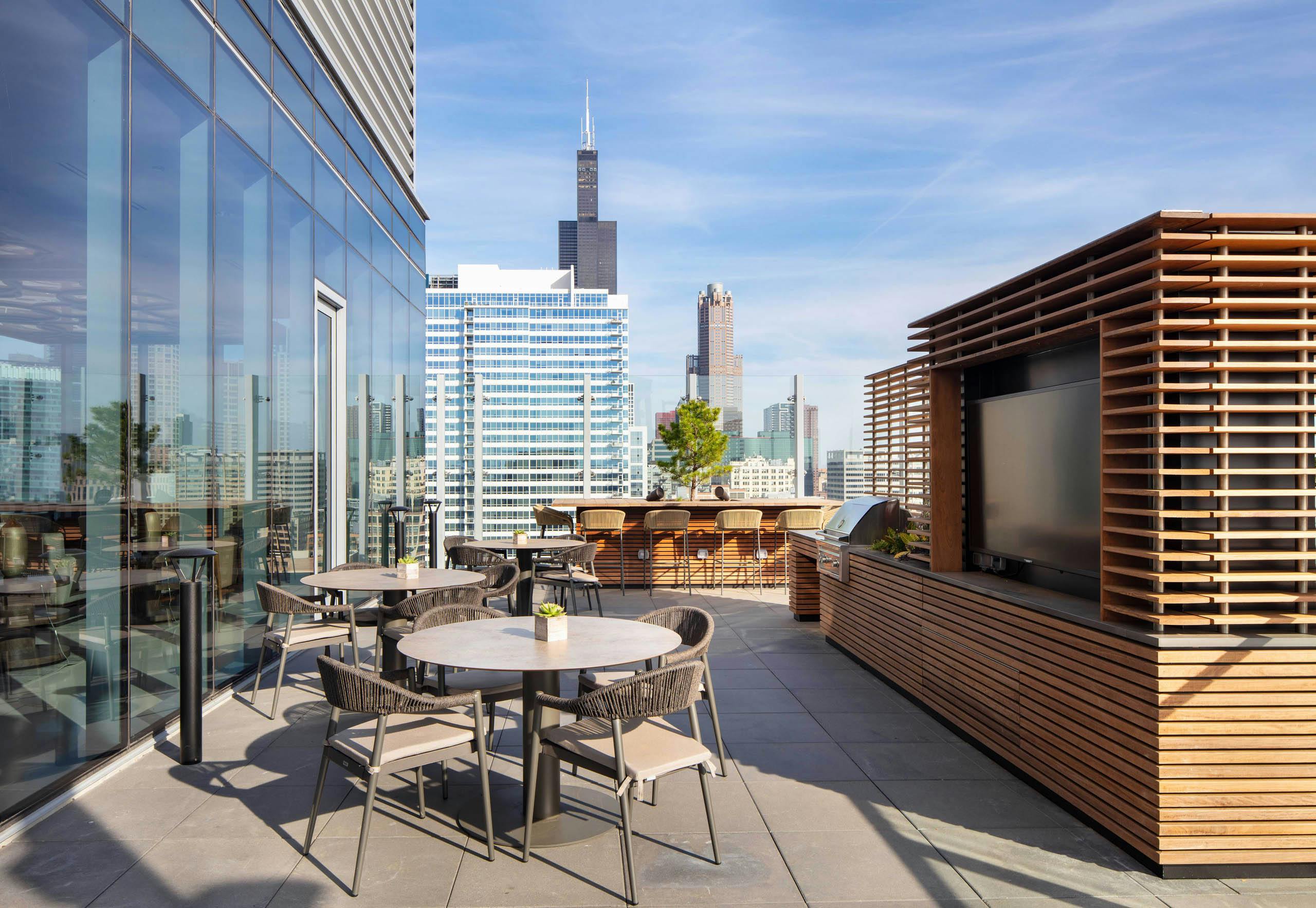 AMLI West Loop spacious rooftop dining area with tables, a grill station, and a view of the city skyline.