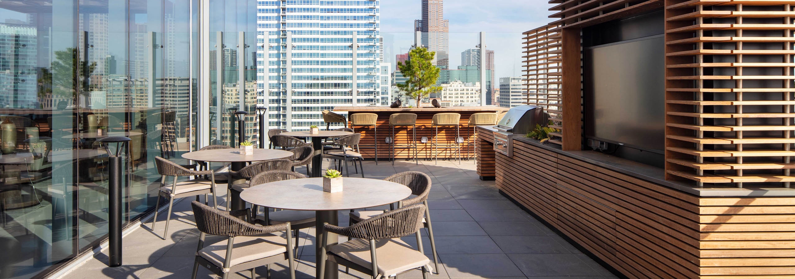 AMLI West Loop spacious rooftop dining area with tables, a grill station, and a view of the city skyline.