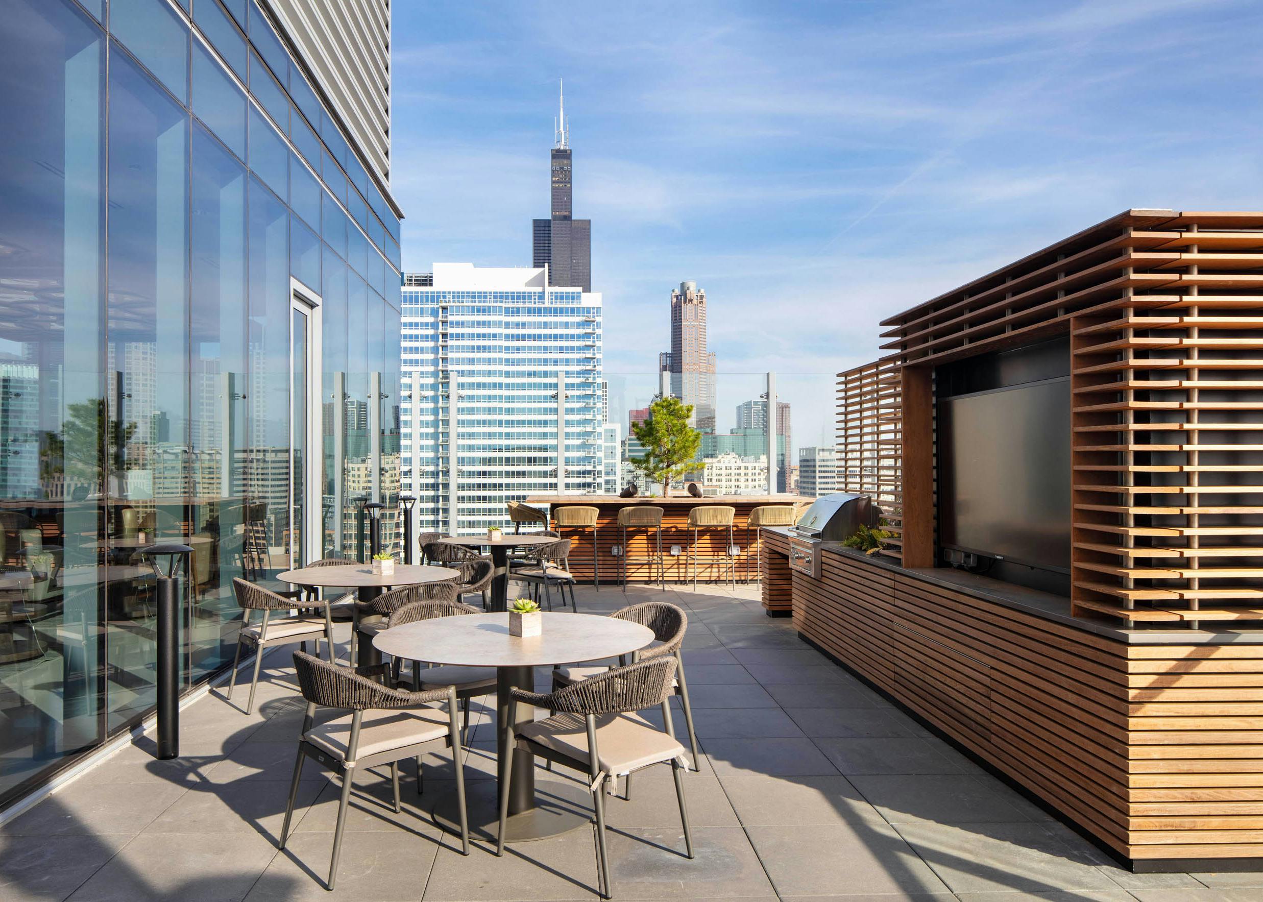 AMLI West Loop spacious rooftop dining area with tables, a grill station, and a view of the city skyline.