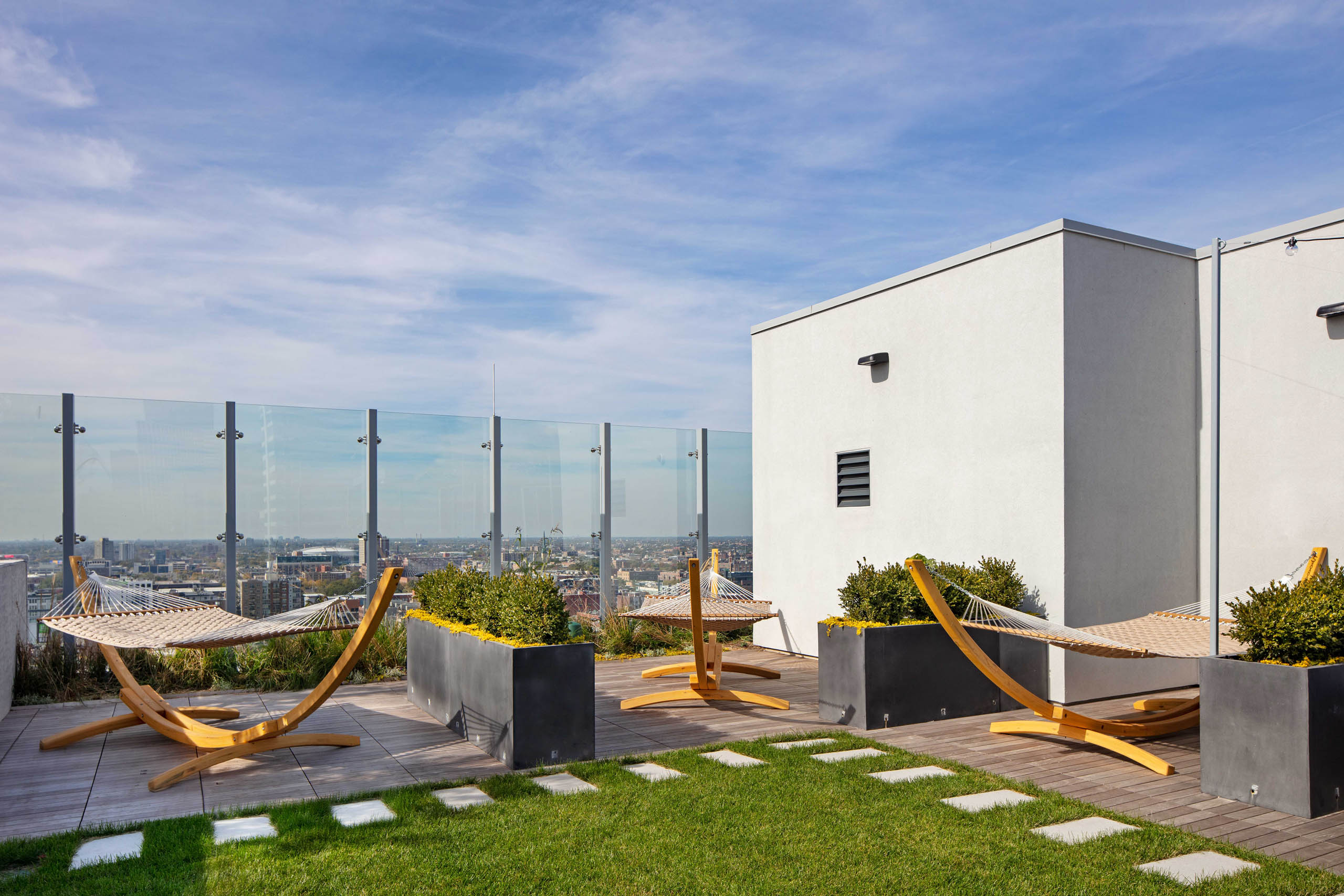Daytime view of AMLI West Loop Rooftop Lounge Area with 3 wooden hammocks, planters, and a small grass area.