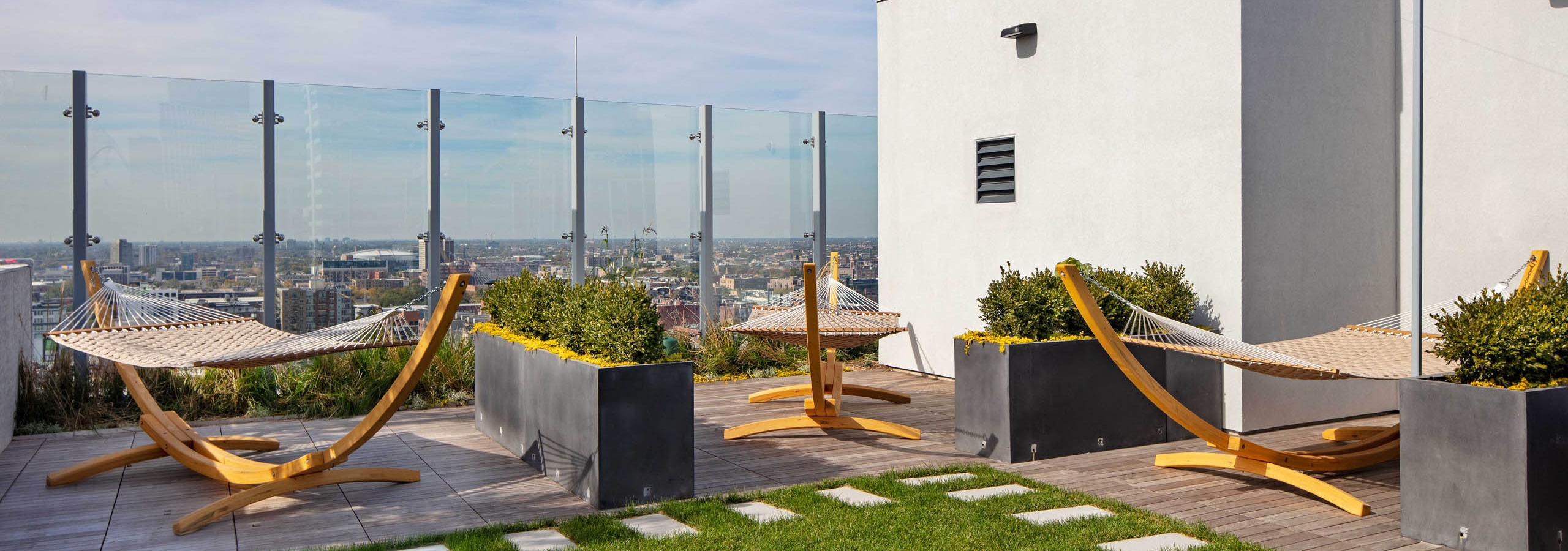 Daytime view of AMLI West Loop Rooftop Lounge Area with 3 wooden hammocks, planters, and a small grass area.
