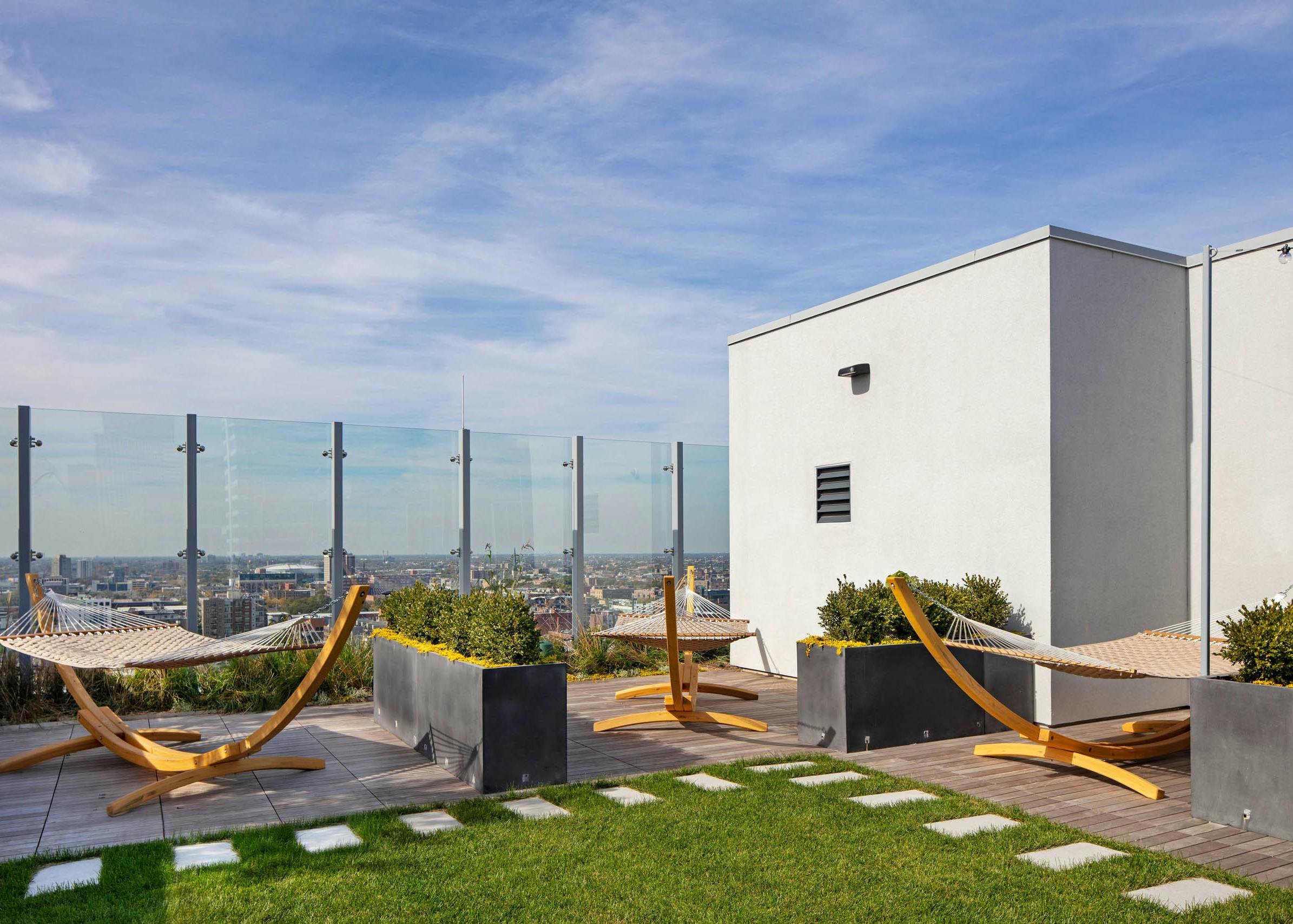 Daytime view of AMLI West Loop Rooftop Lounge Area with 3 wooden hammocks, planters, and a small grass area.