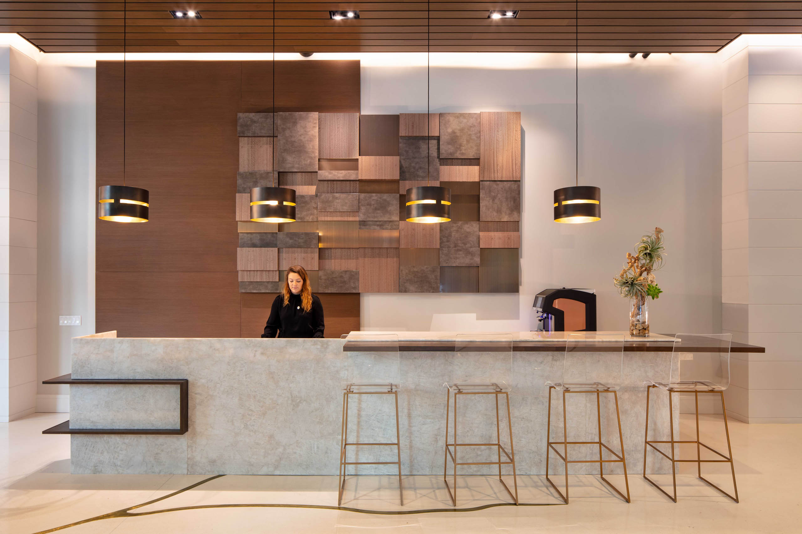 AMLI West Loop modern lobby with a concierge desk, featuring a woman standing behind it, contemporary pendant lights, and decorative wood paneling.
