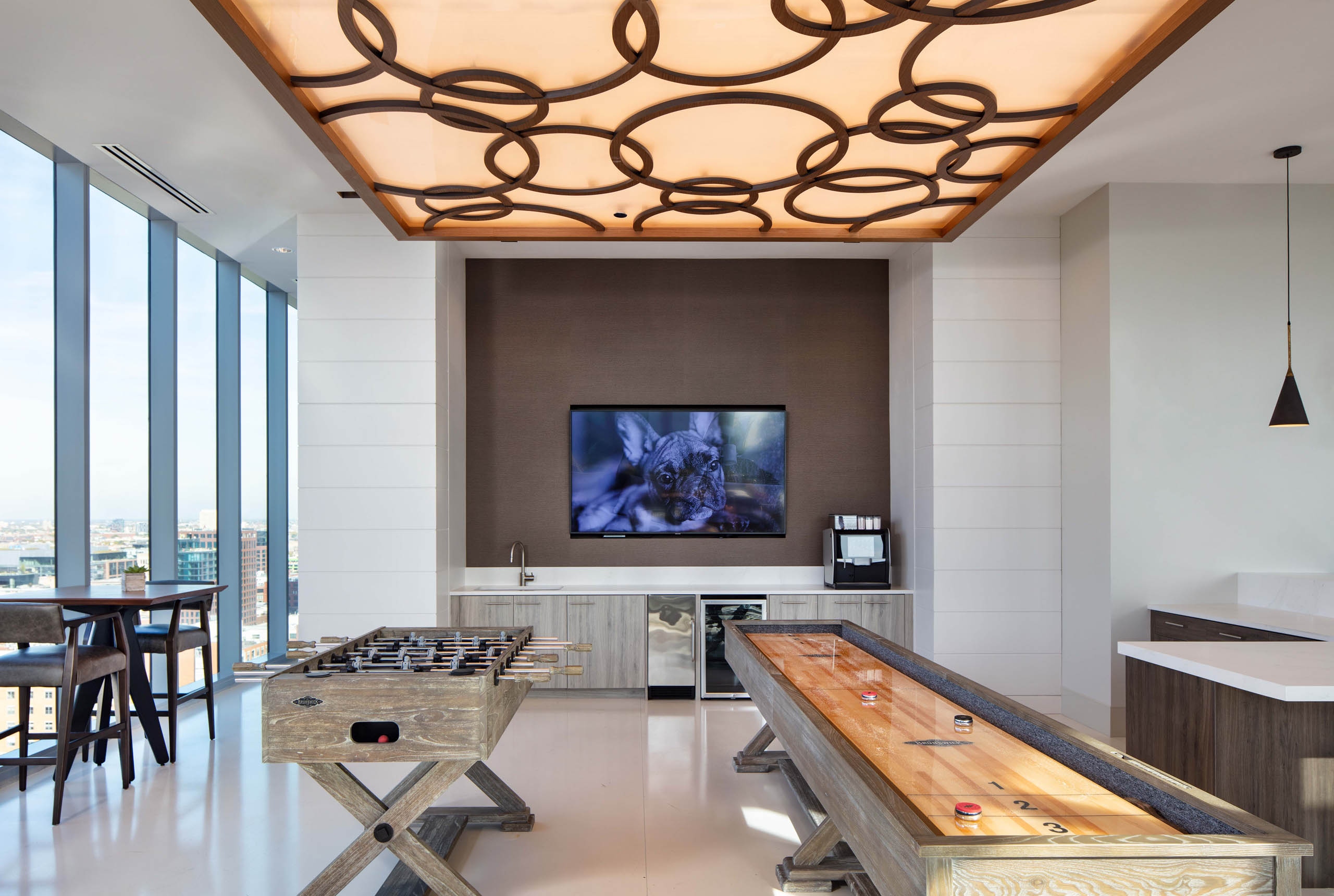 Interior shot of the Resident Lounge game area with foosball and shuffleboard tables, a built-in counter, TV, and large windows at AMLI West Loop
