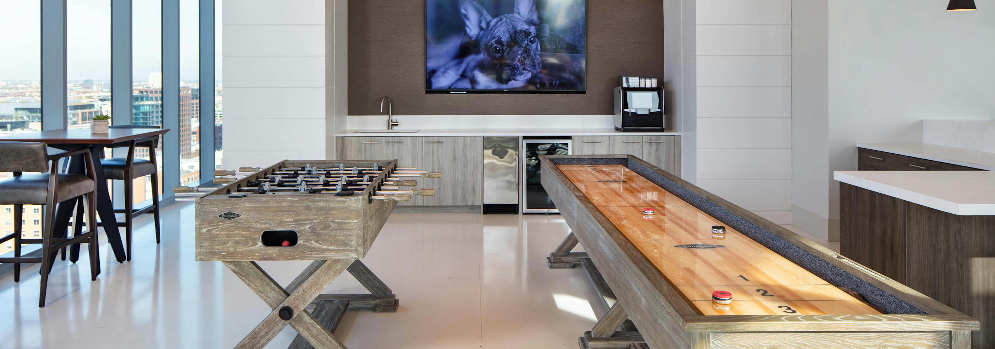 Interior shot of the Resident Lounge game area with foosball and shuffleboard tables, a built-in counter, TV, and large windows at AMLI West Loop