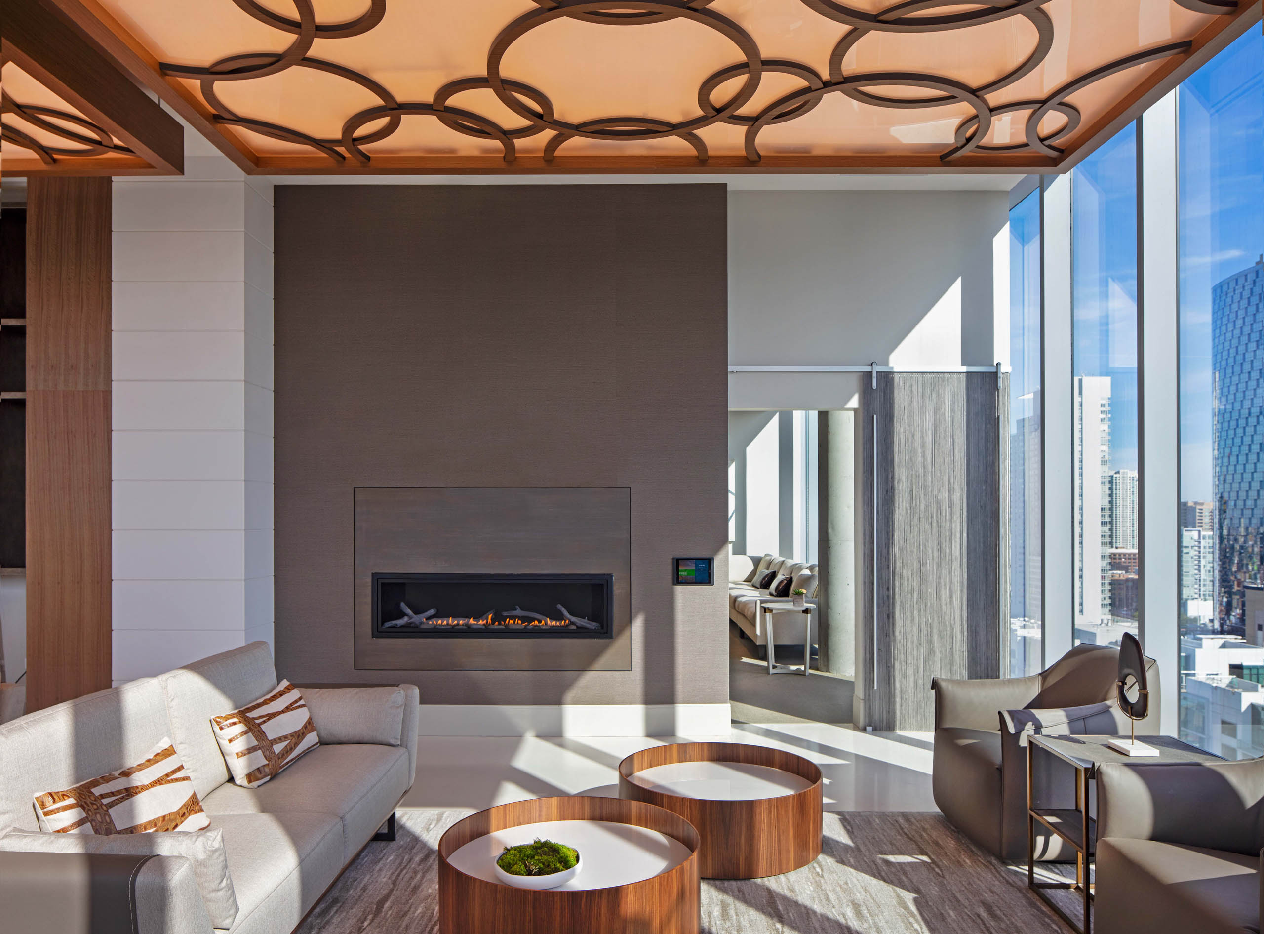 Interior view of AMLI West Loop Resident Lounge with a large fireplace and a gray couch and chairs with a modern ceiling.
