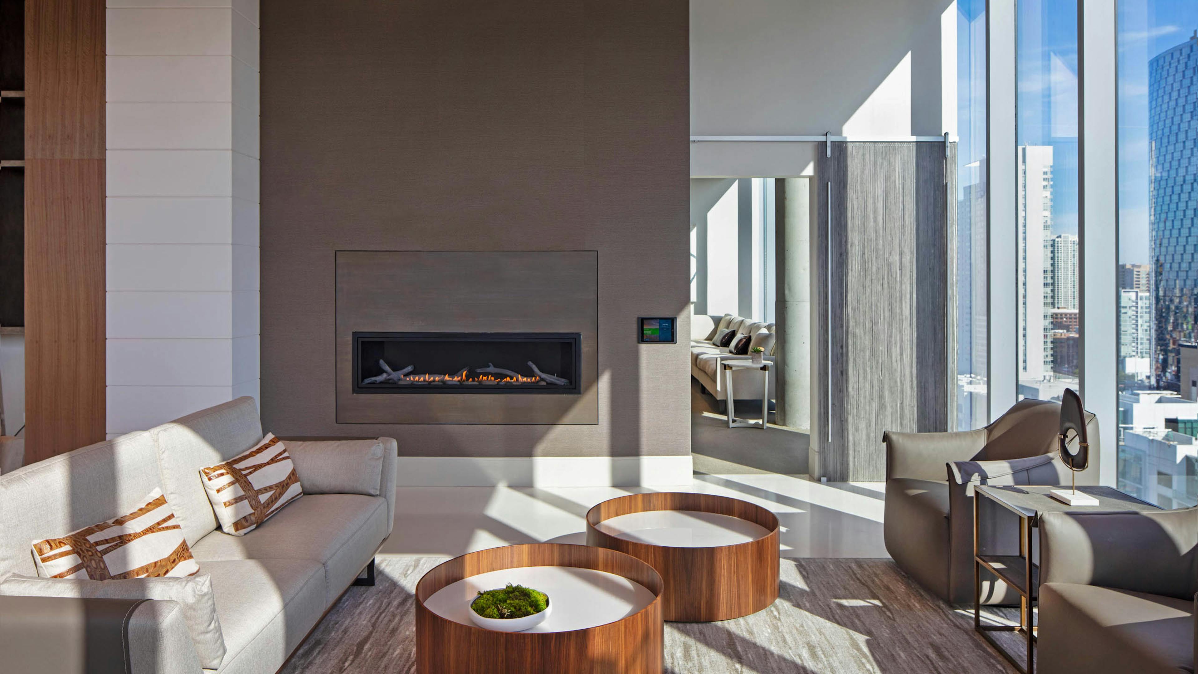 Interior view of AMLI West Loop Resident Lounge with a large fireplace and a gray couch and chairs with a modern ceiling.