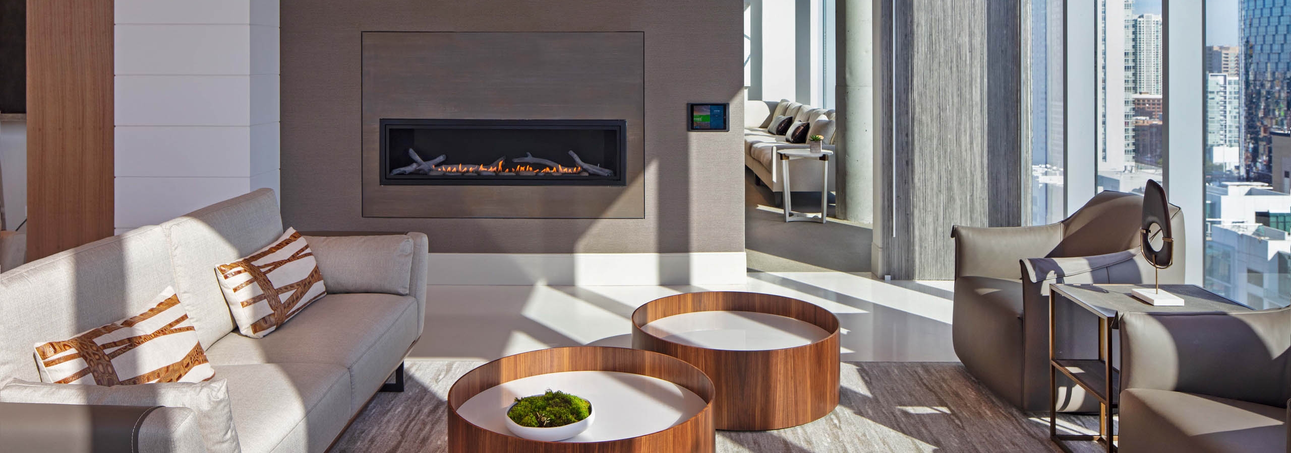 Interior view of AMLI West Loop Resident Lounge with a large fireplace and a gray couch and chairs with a modern ceiling.