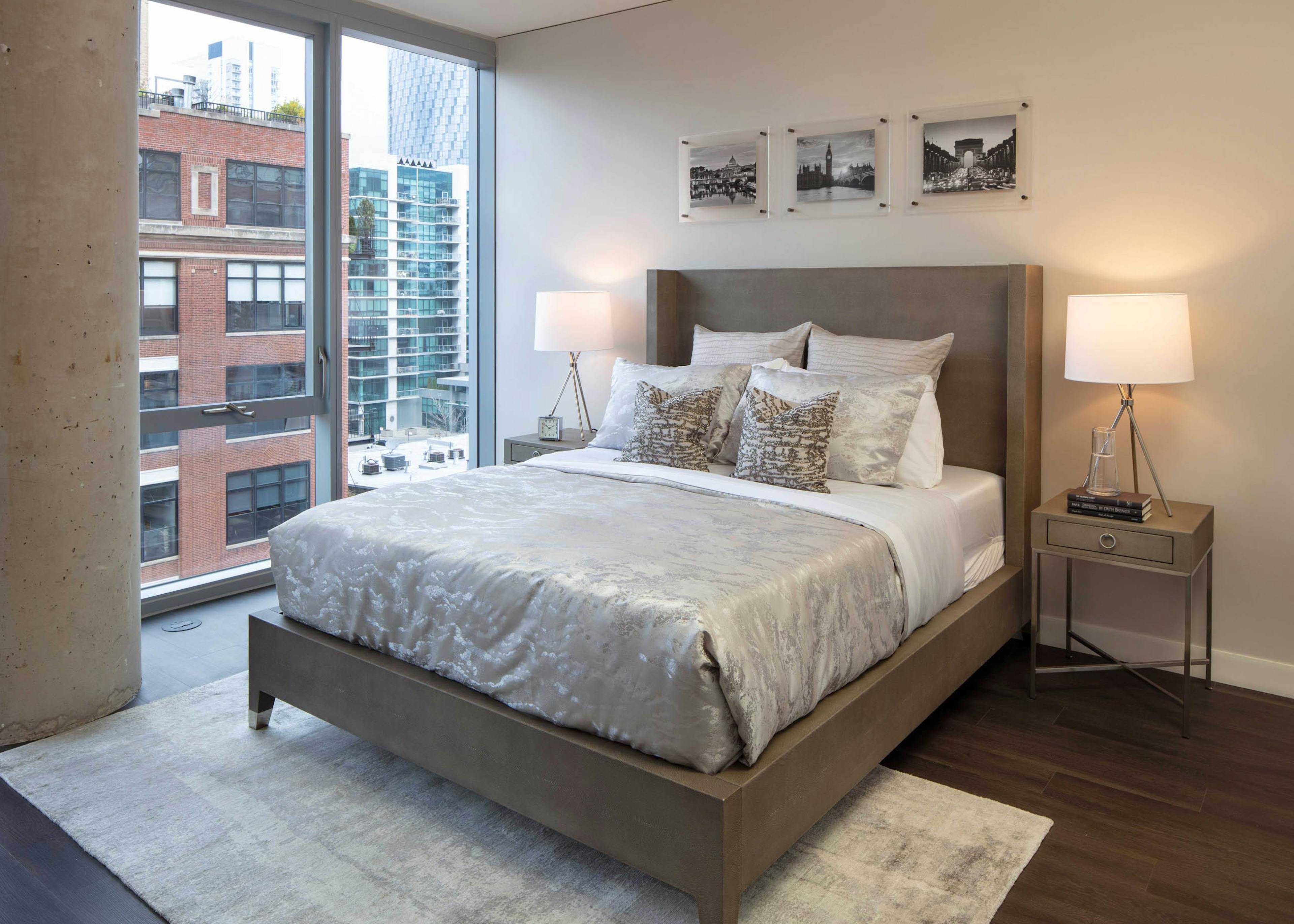 AMLI West Loop bedroom with a large bed, two nightstands and lamps, dark flooring, and floor-to-ceiling windows with a city view.