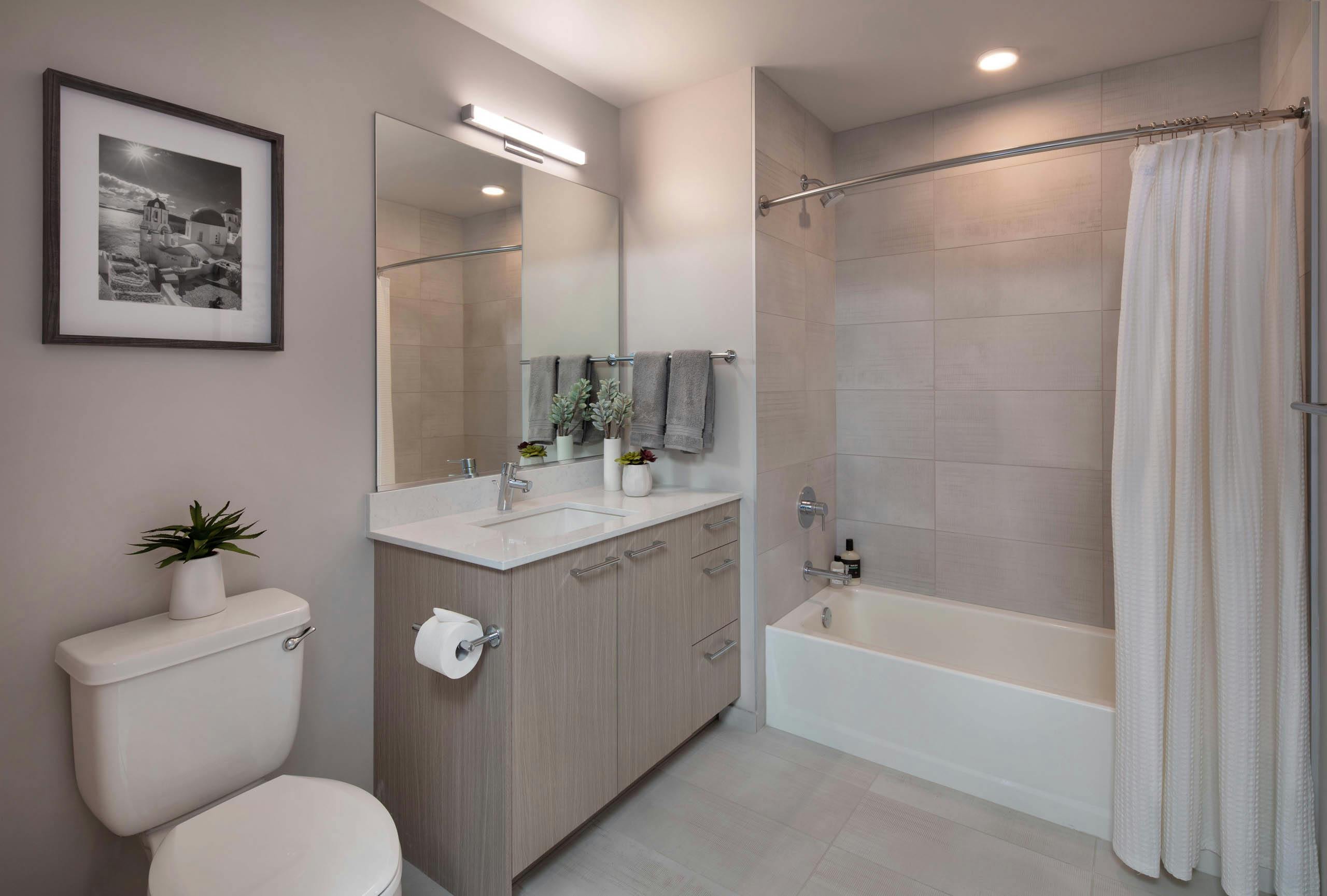 Bathroom at AMLI West Loop with black and white artwork and light wood cabinet and a white bathtub with a shower curtain and oversized tile