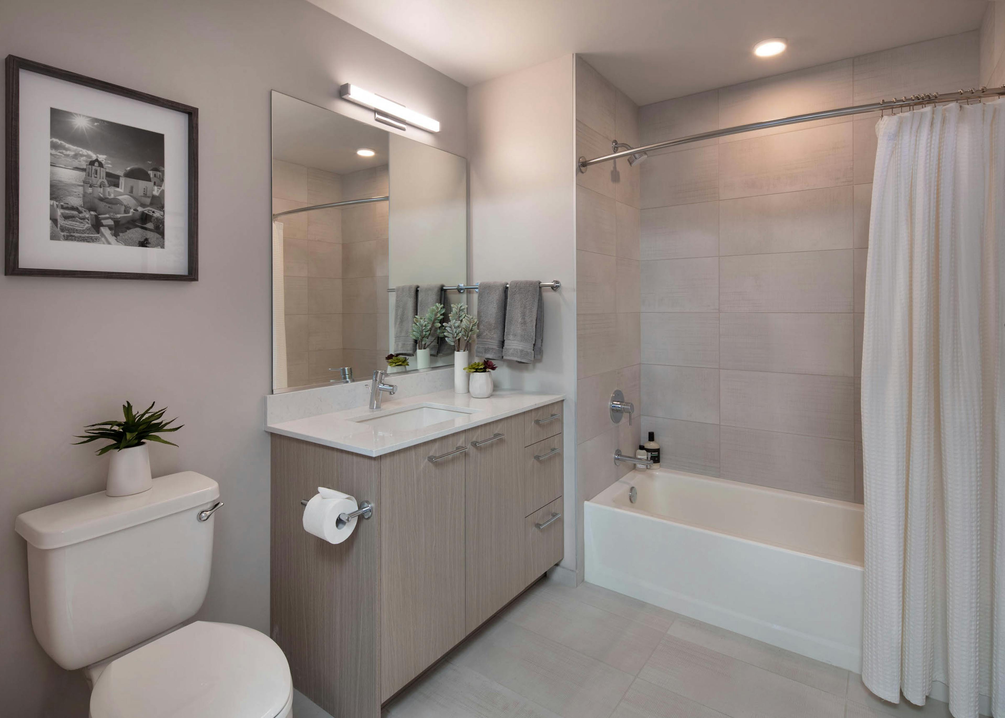 Bathroom at AMLI West Loop with black and white artwork and light wood cabinet and a white bathtub with a shower curtain and oversized tile