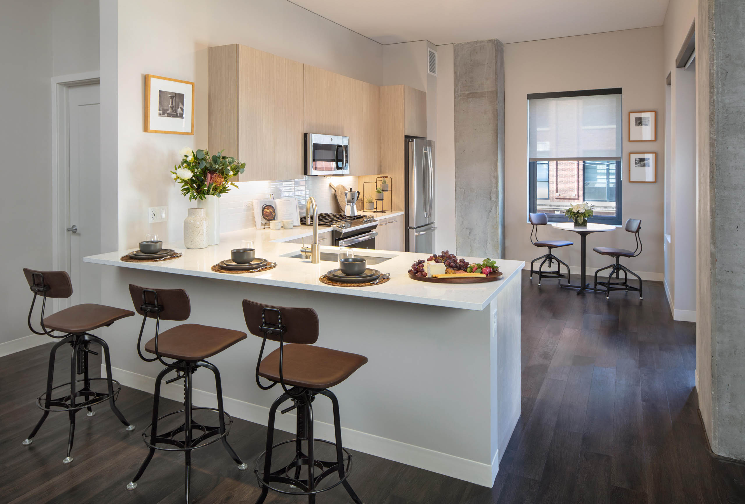 Kitchen at AMLI West Loop featuring light wood cabinetry, stainless steel appliances, a white counter peninsula with bar stools, and a small dining nook