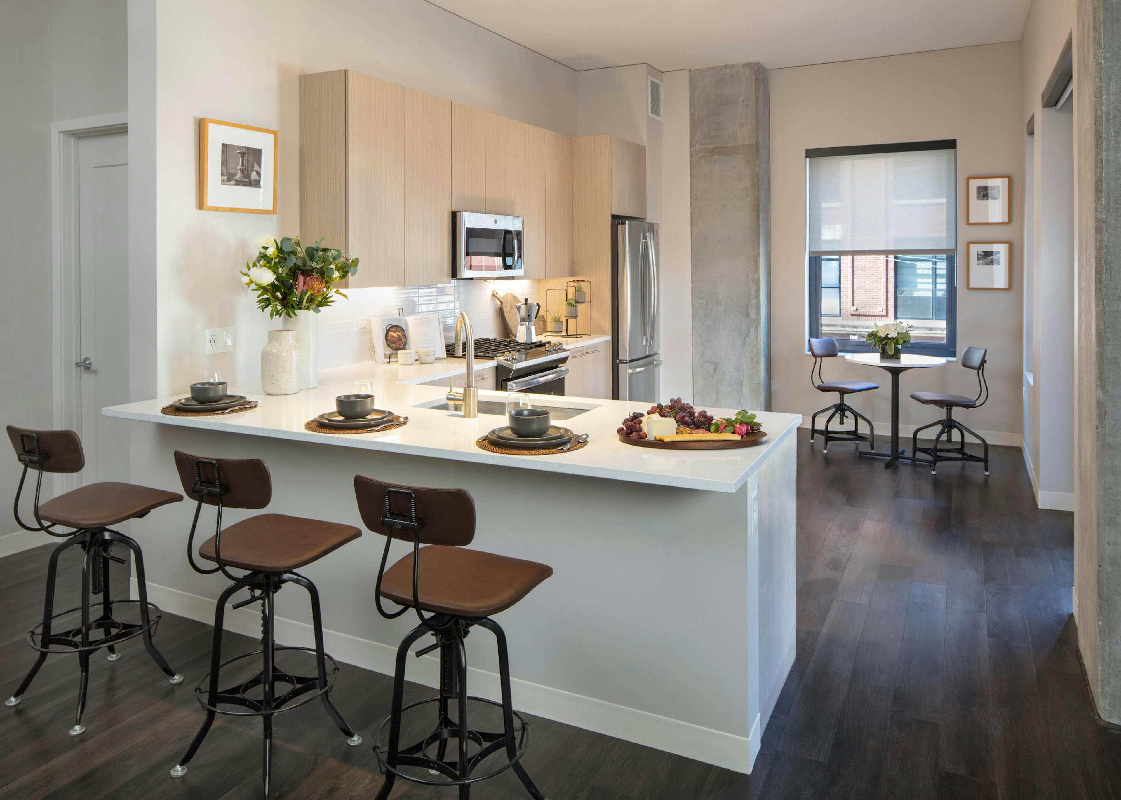 Kitchen at AMLI West Loop featuring light wood cabinetry, stainless steel appliances, a white counter peninsula with bar stools, and a small dining nook