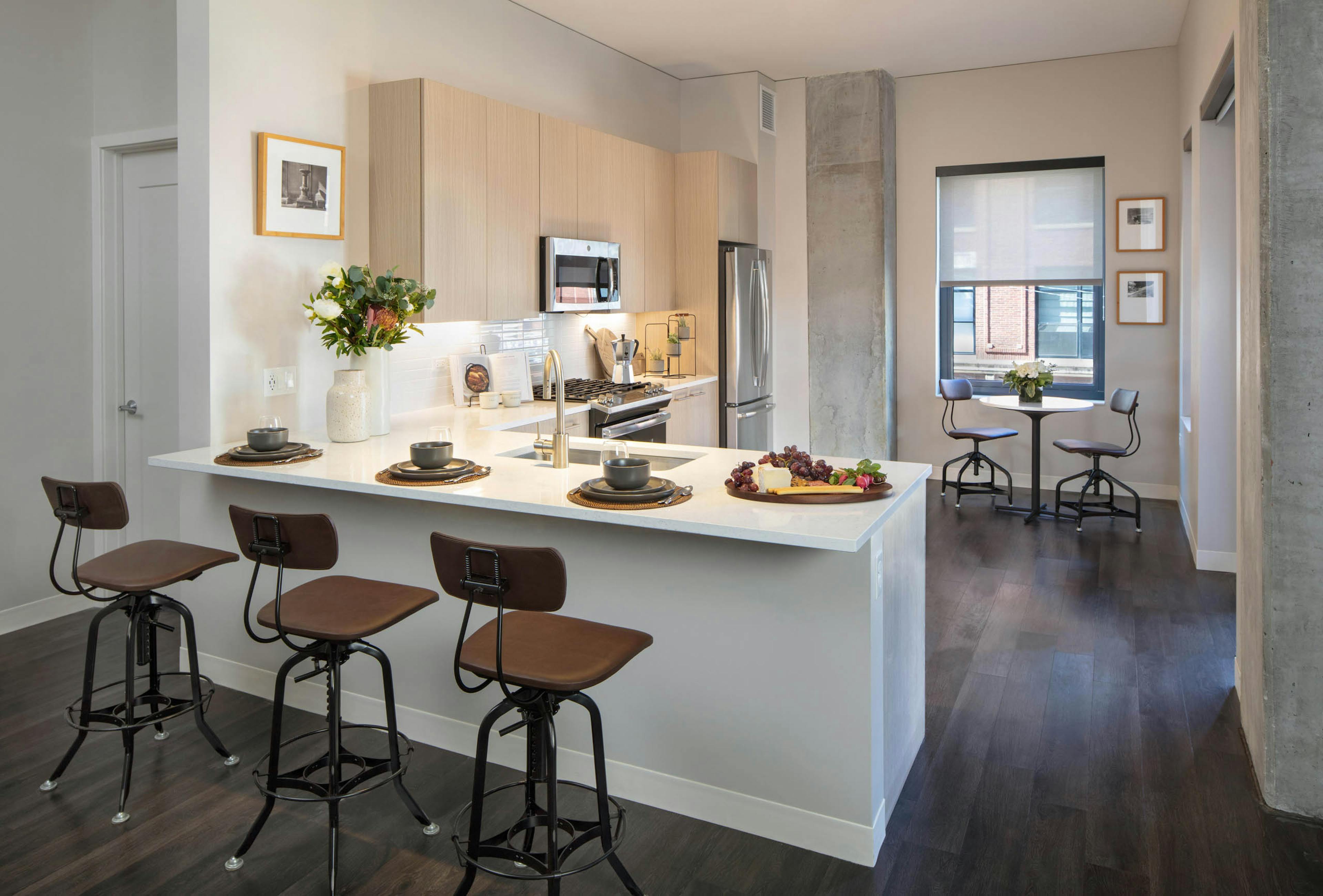 Kitchen at AMLI West Loop featuring light wood cabinetry, stainless steel appliances, a white counter peninsula with bar stools, and a small dining nook