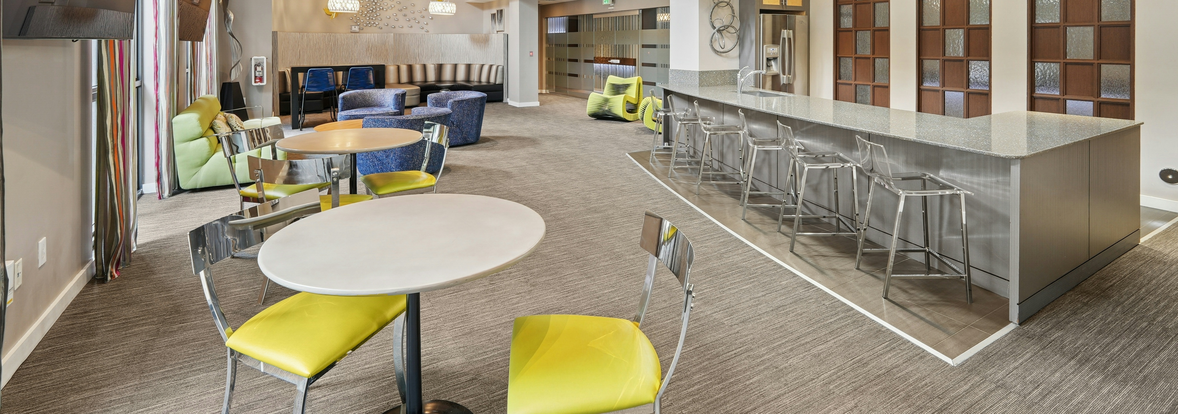 Resident clubroom at AMLI Dadeland apartments featuring a long quartz bar top with stools and couches and smaller tables