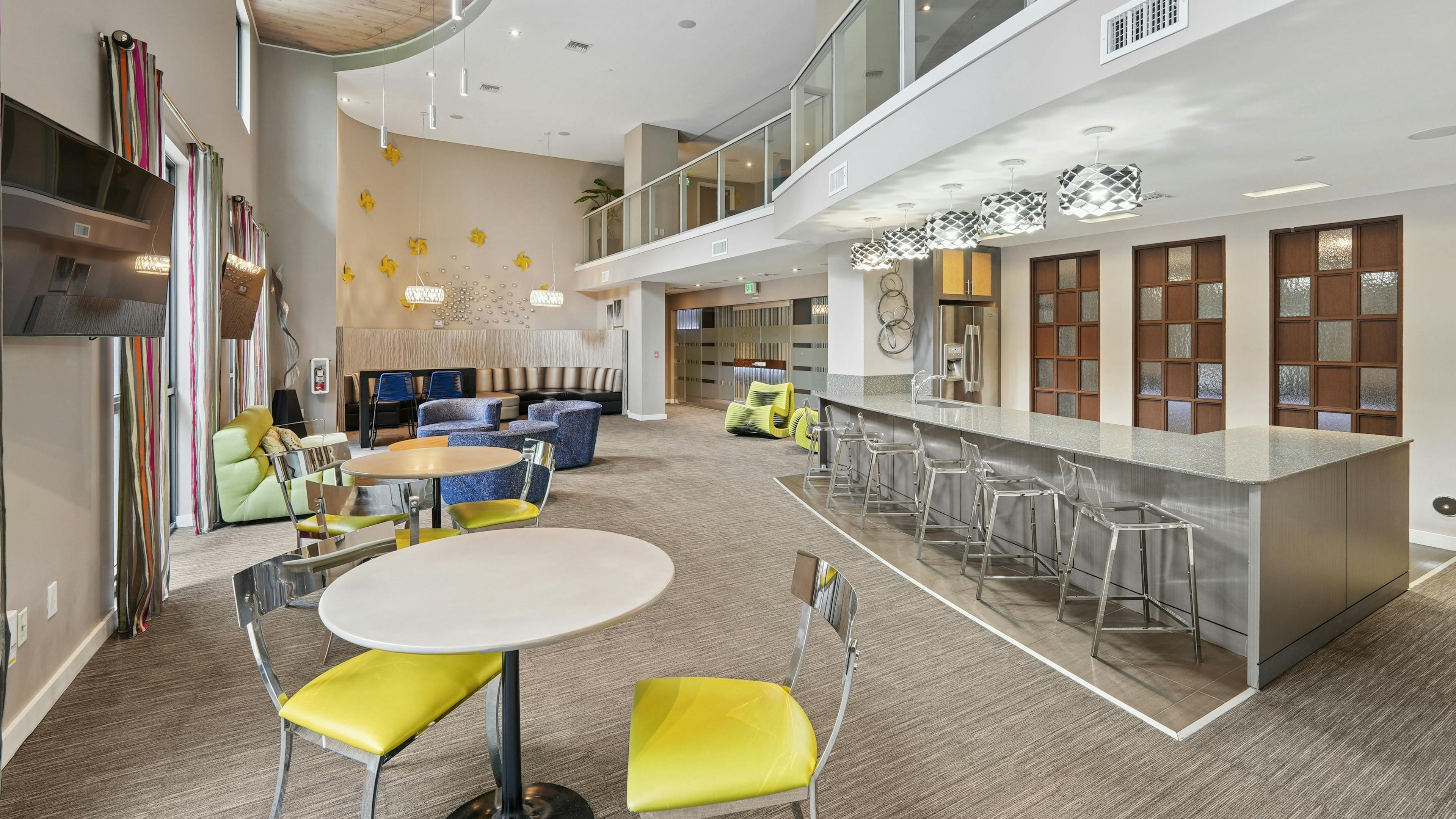 Resident clubroom at AMLI Dadeland apartments featuring a long quartz bar top with stools and couches and smaller tables