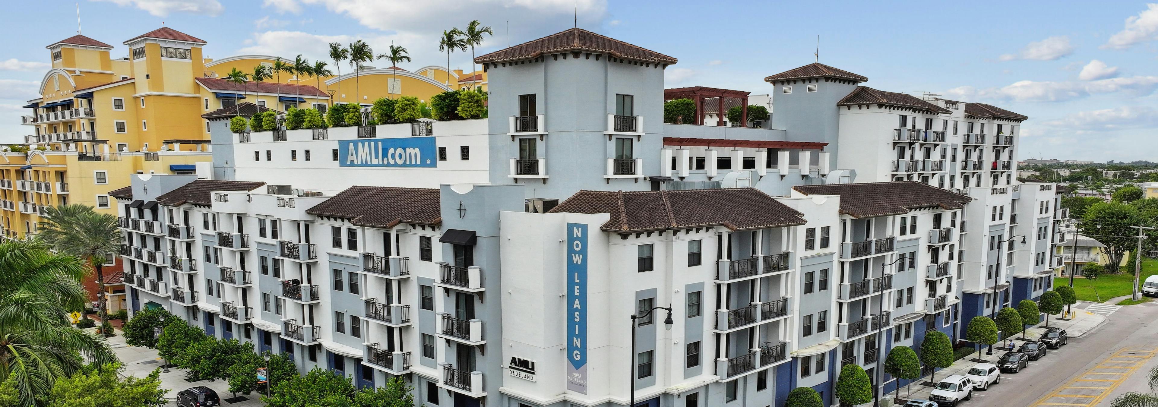 Exterior view of the AMLI Dadeland apartment building with seven floors and street parking and trees and blue sky with clouds
