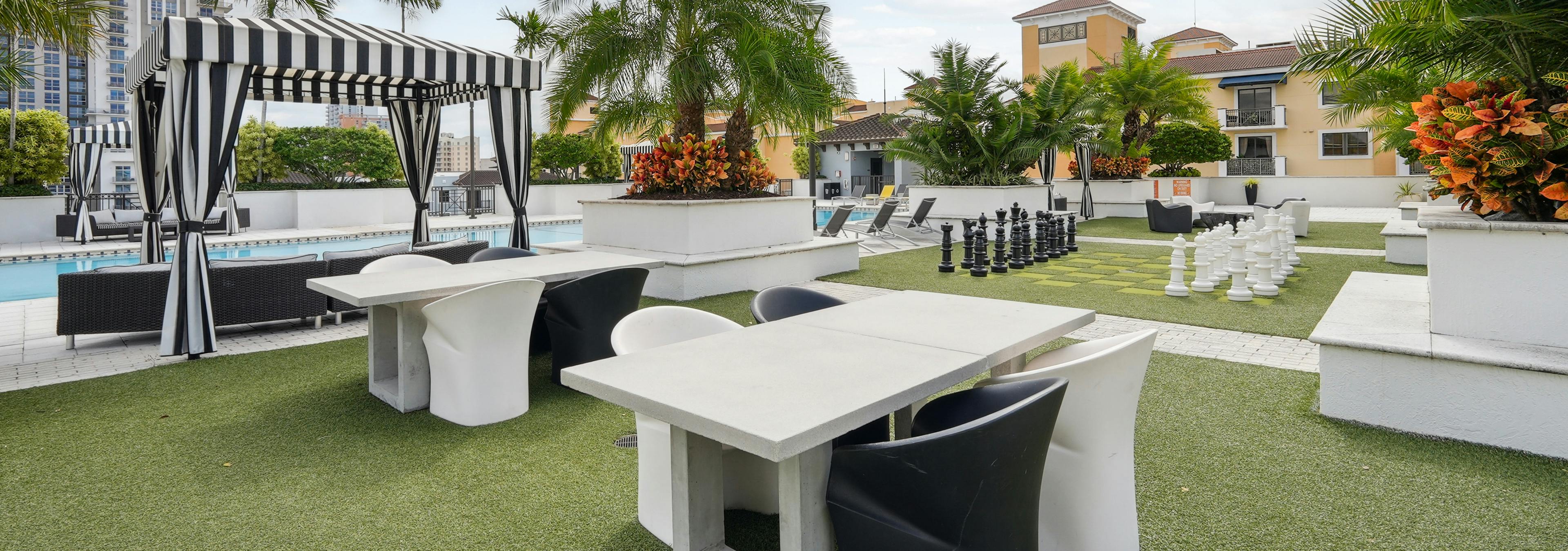 Exterior view of the rooftop amenity space at AMLI Dadeland with a swimming pool and several seating areas and palm trees
