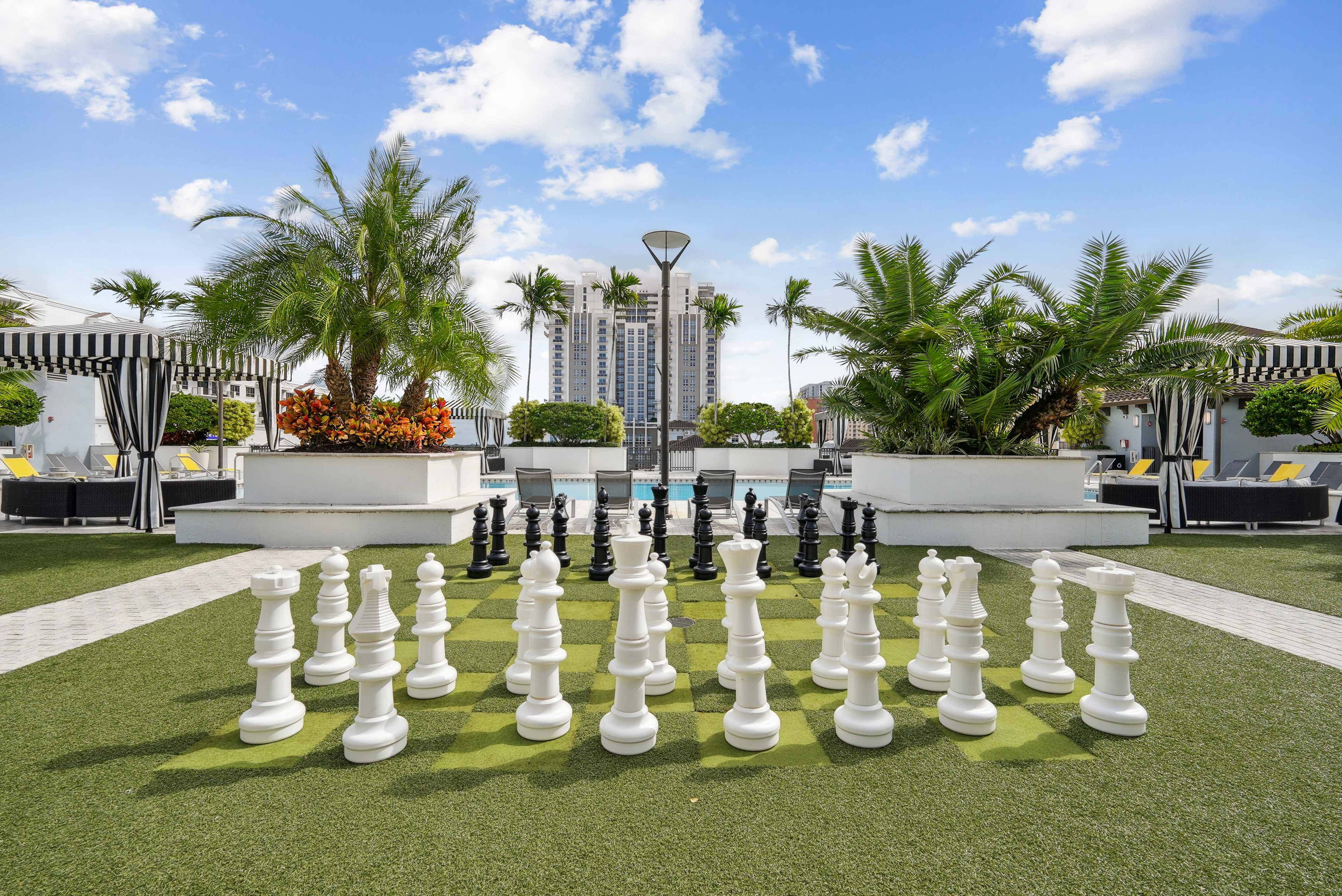 Lounge area at AMLI Dadeland apartments with a giant chess board on artificial green turf and a view of the swimming pool