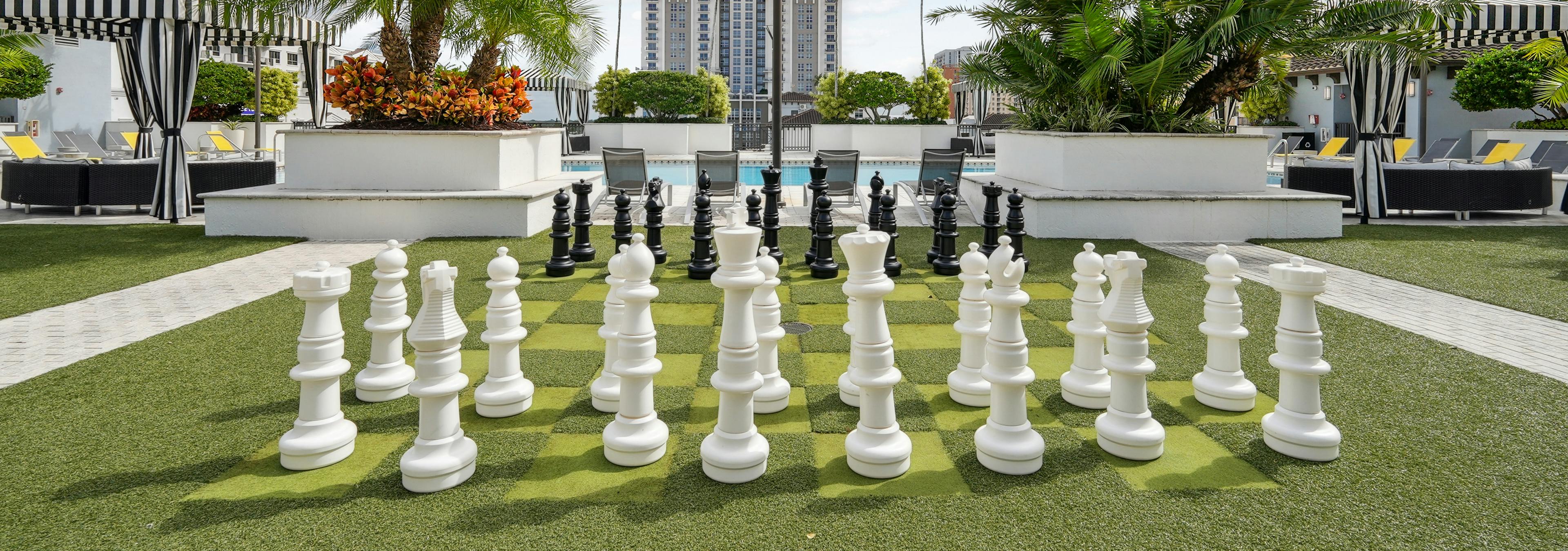 Lounge area at AMLI Dadeland apartments with a giant chess board on artificial green turf and a view of the swimming pool