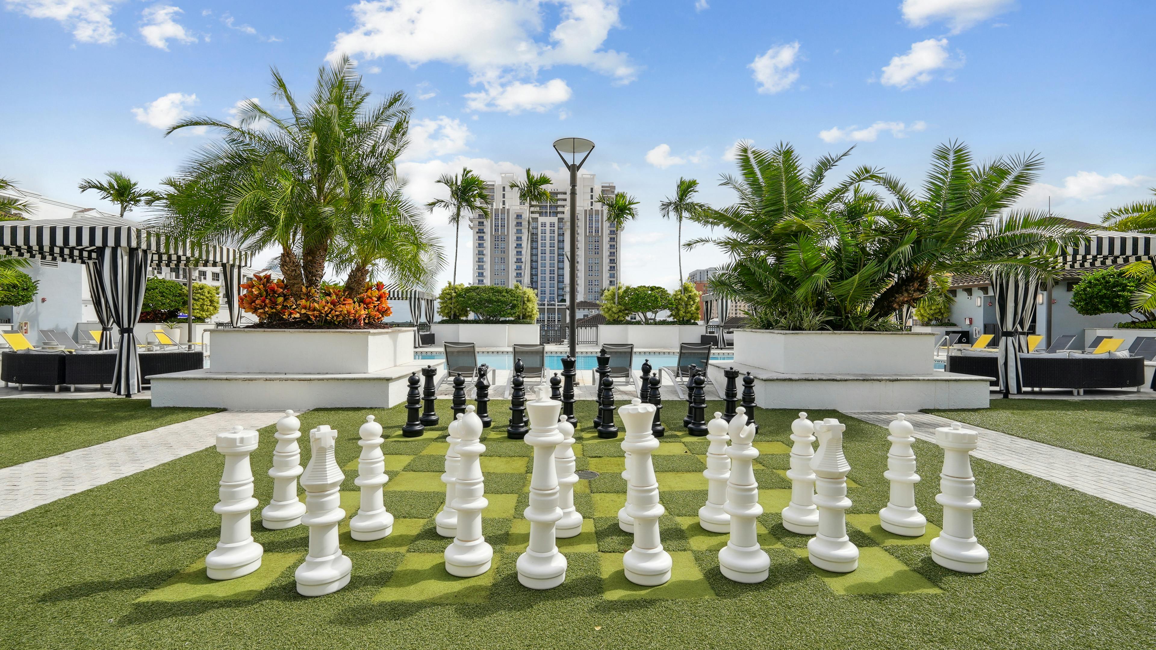 Lounge area at AMLI Dadeland apartments with a giant chess board on artificial green turf and a view of the swimming pool