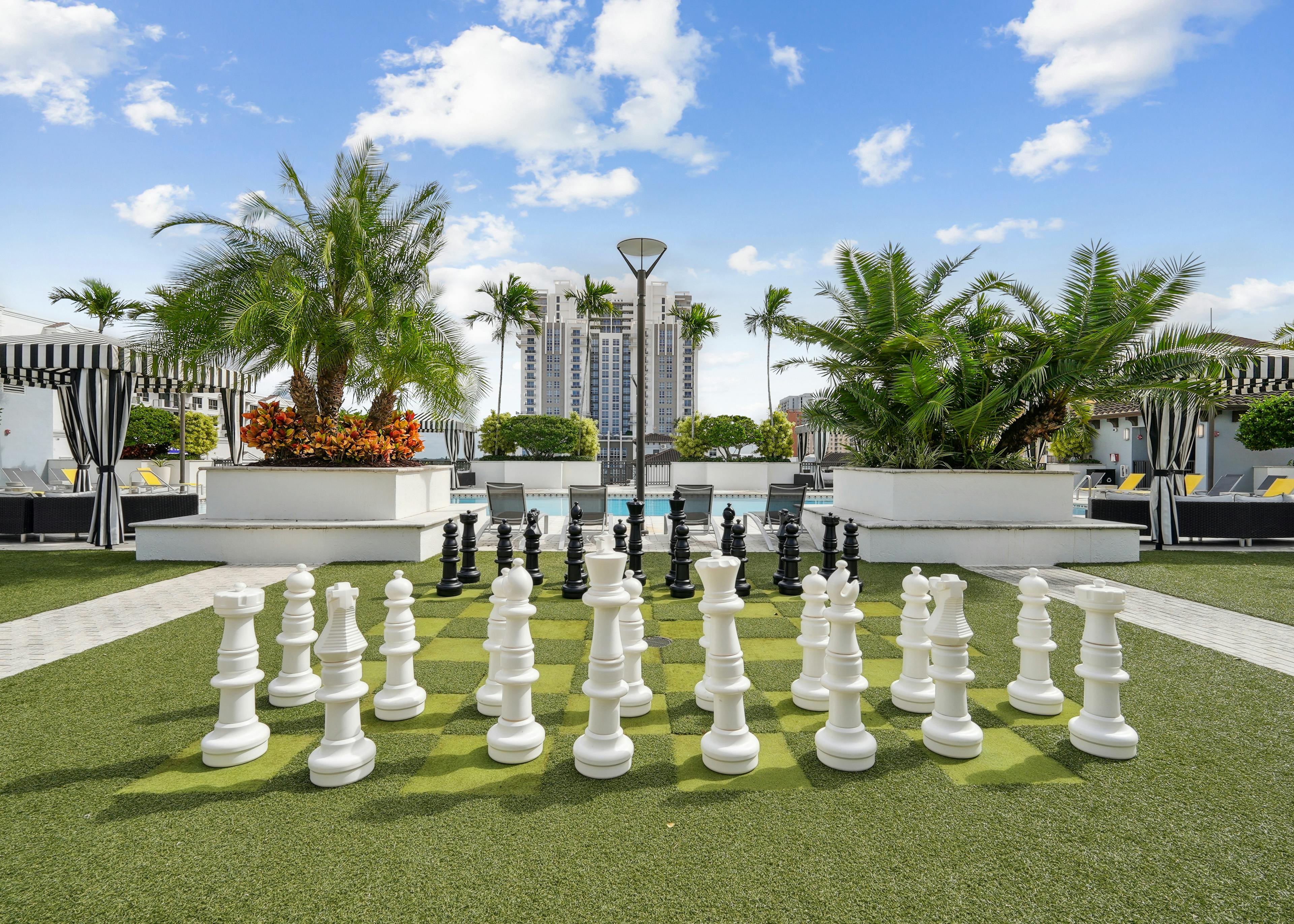 Lounge area at AMLI Dadeland apartments with a giant chess board on artificial green turf and a view of the swimming pool
