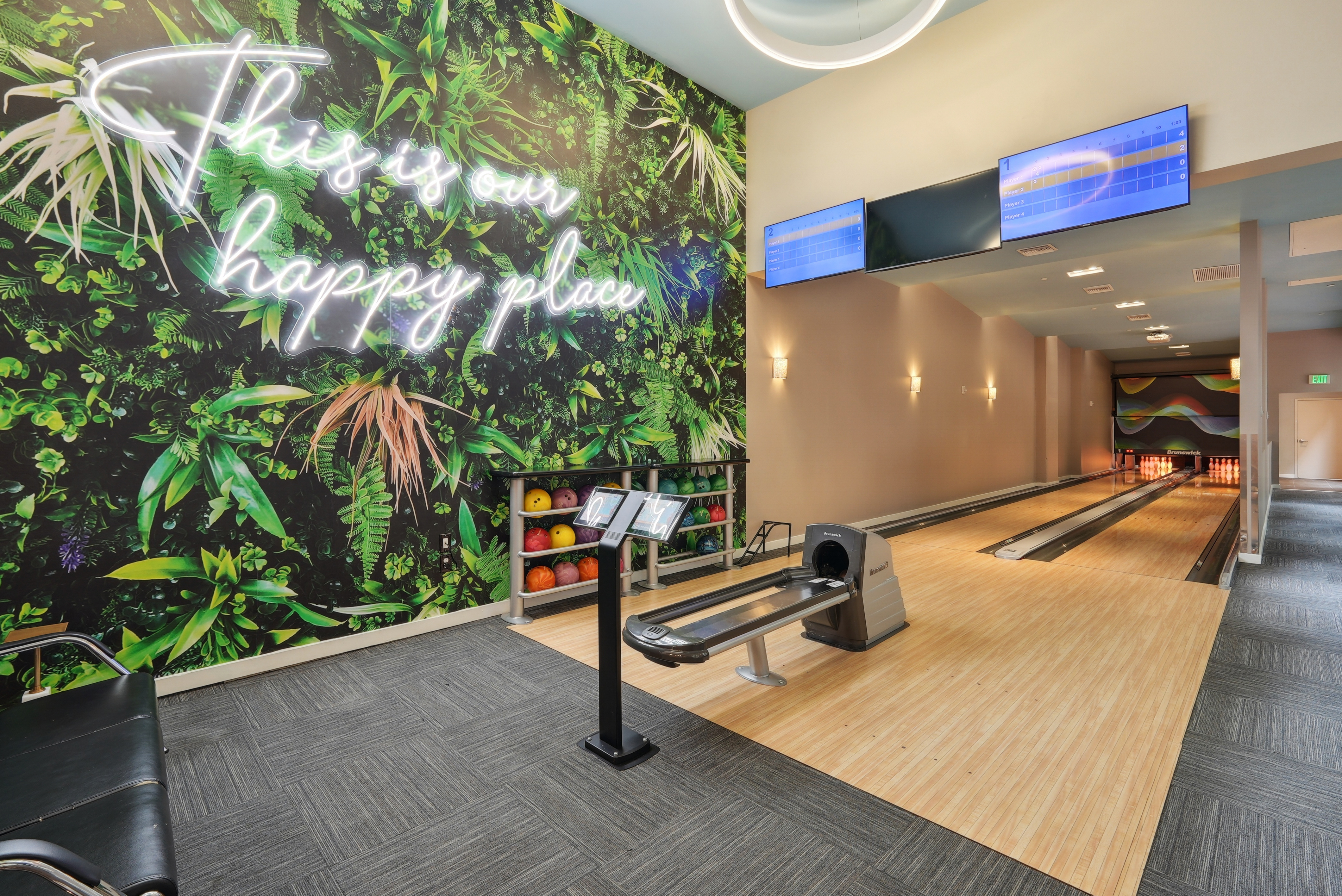 Bowling alley at AMLI Dadeland apartments with two lanes and several bowling balls and a wall mural featuring green plants