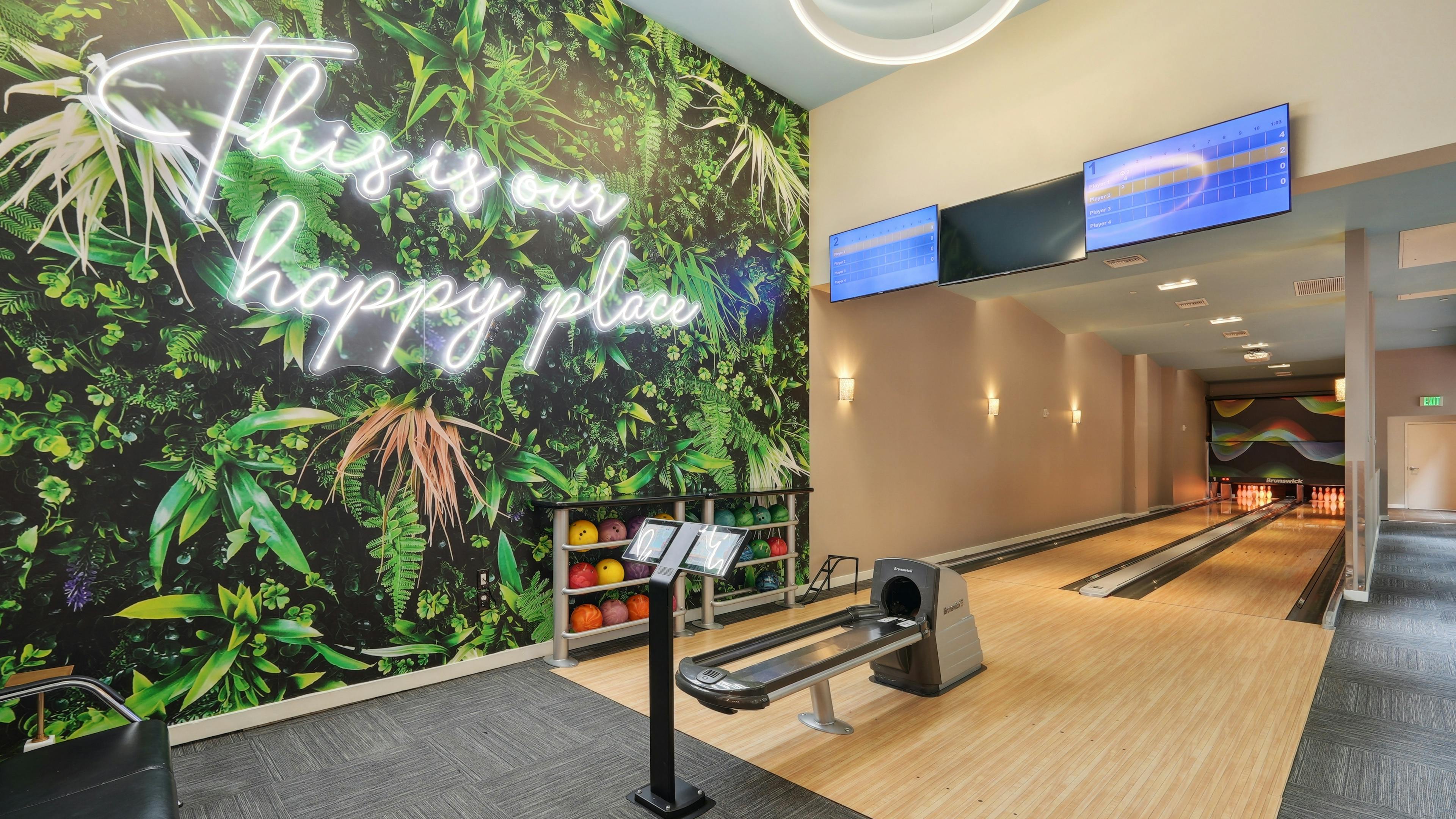 Bowling alley at AMLI Dadeland apartments with two lanes and several bowling balls and a wall mural featuring green plants