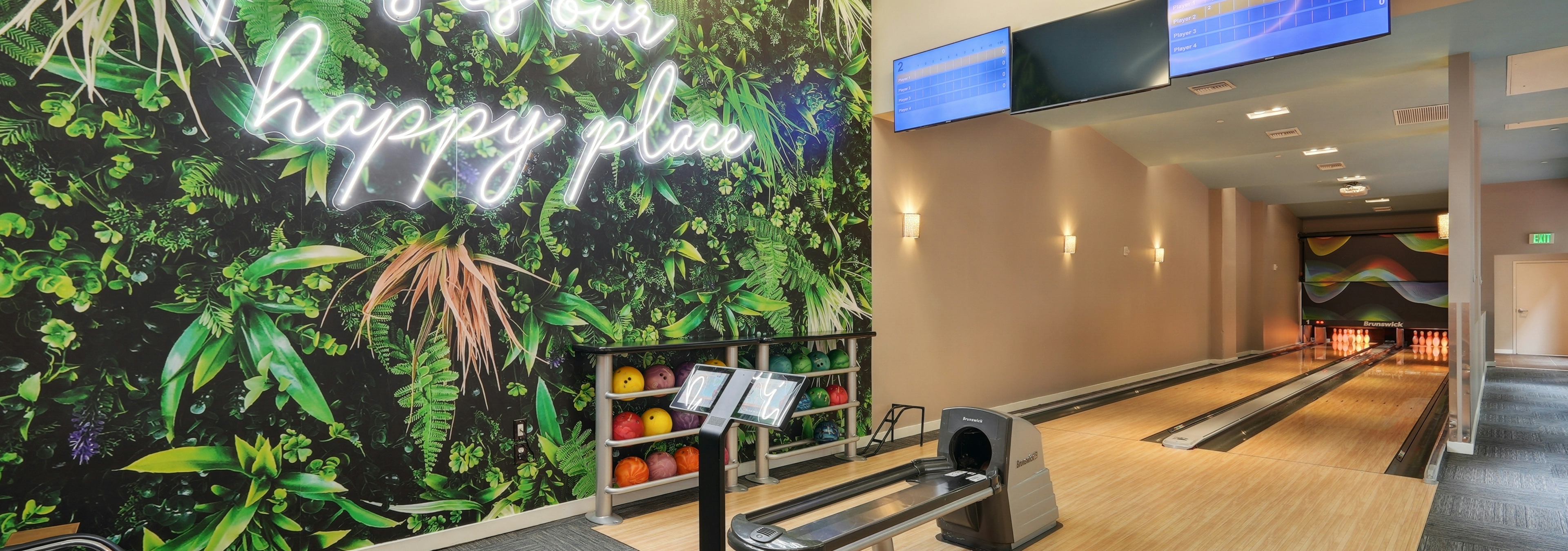 Bowling alley at AMLI Dadeland apartments with two lanes and several bowling balls and a wall mural featuring green plants