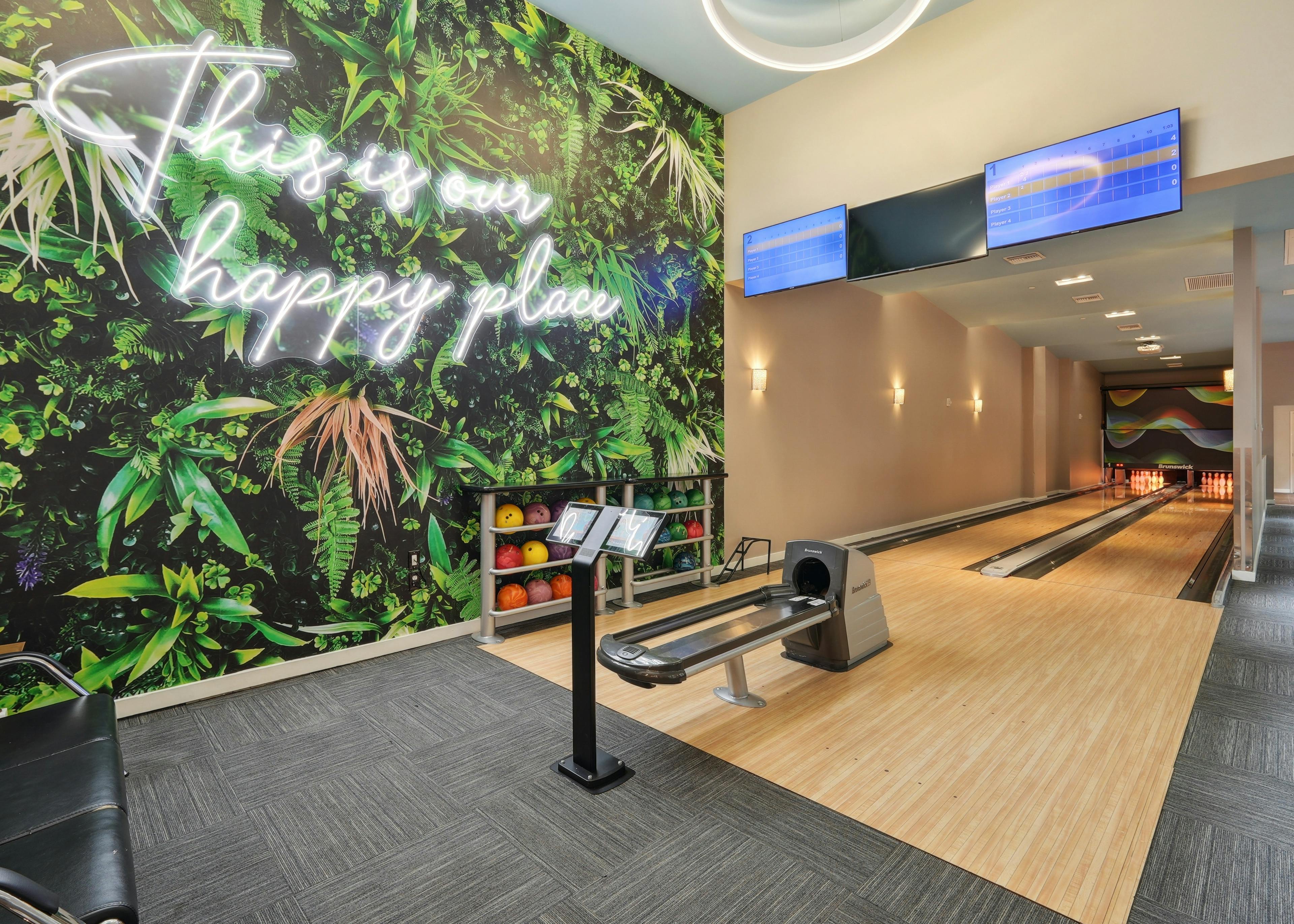 Bowling alley at AMLI Dadeland apartments with two lanes and several bowling balls and a wall mural featuring green plants