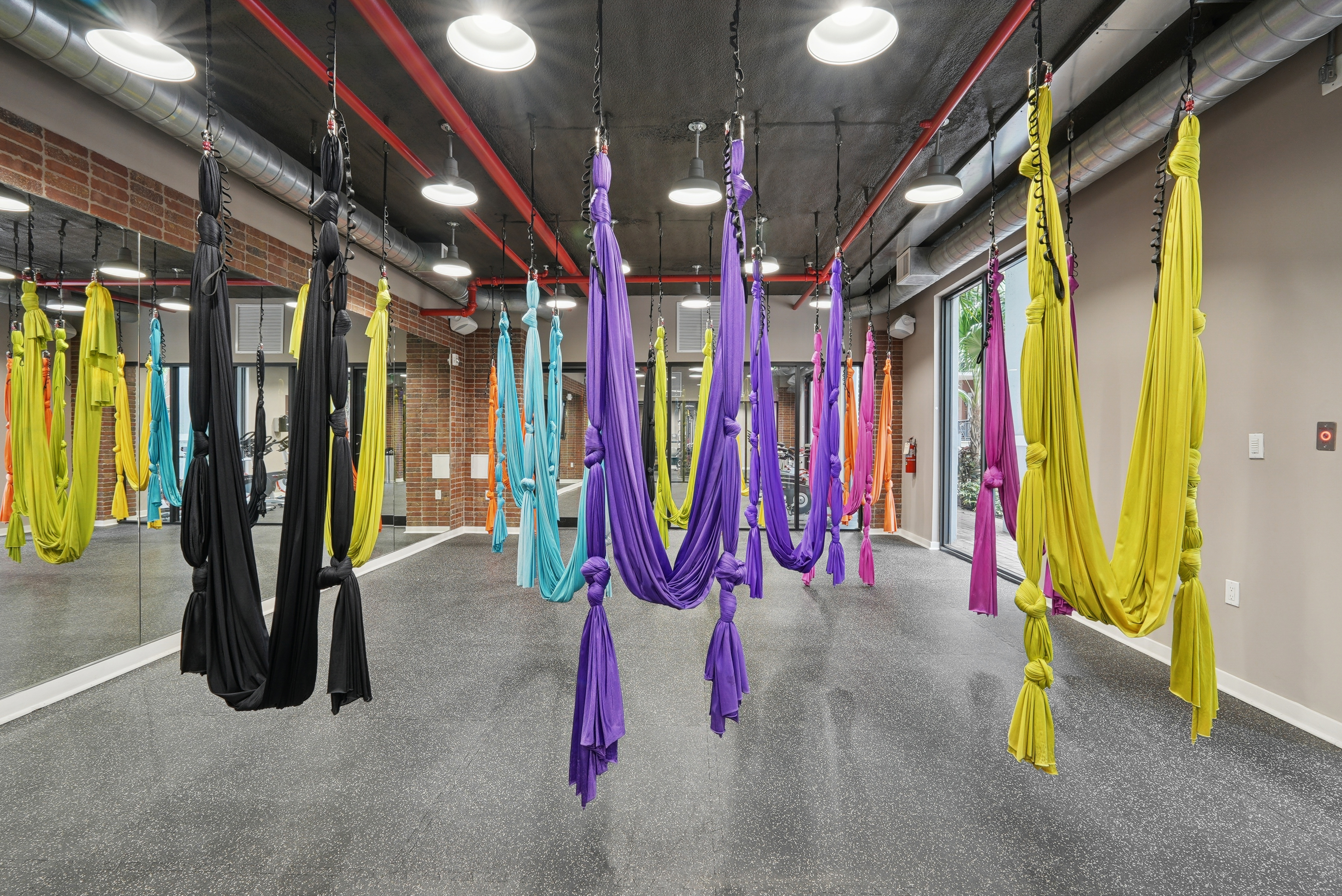 Interior view of an aerial yoga studio with hardwood flooring and floor to ceiling mirrors and a natural brick wall