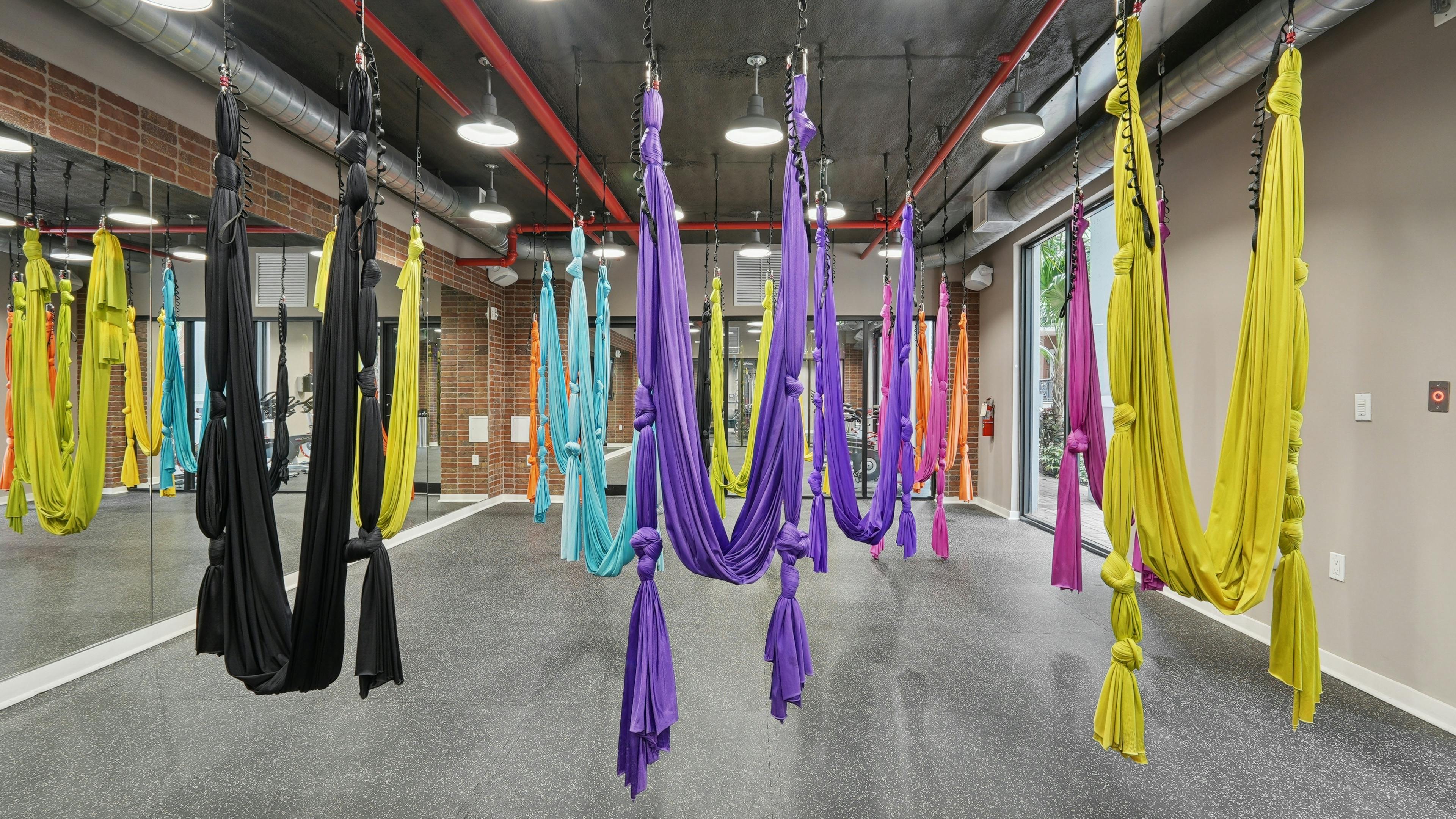 Interior view of an aerial yoga studio with hardwood flooring and floor to ceiling mirrors and a natural brick wall