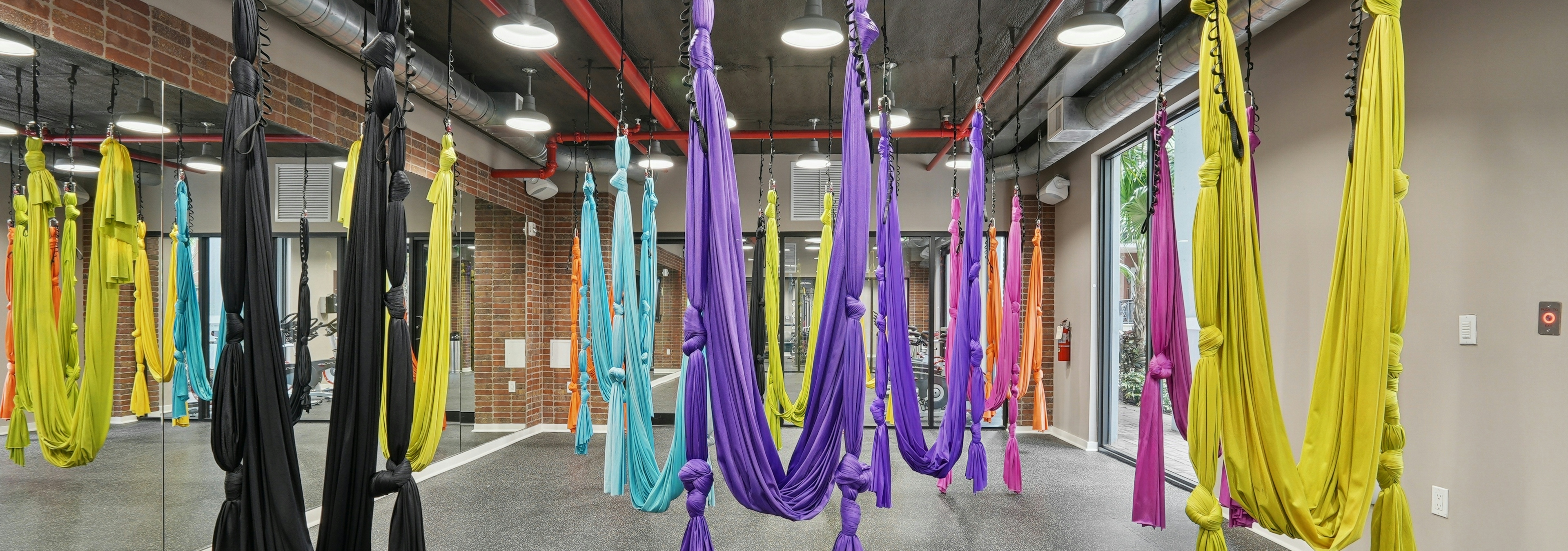 Interior view of an aerial yoga studio with hardwood flooring and floor to ceiling mirrors and a natural brick wall